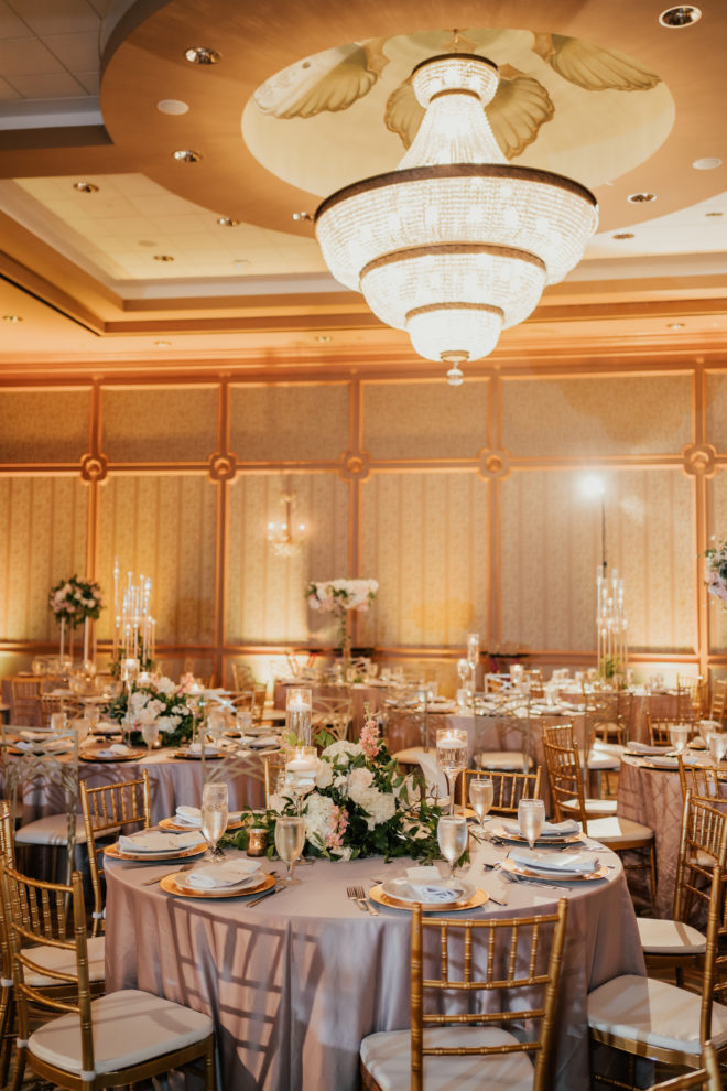 Banquet tables with blush linens, set with ivory, blush and greenery florals, gold tablesettings and gold chivari chairs at a wedding reception at The San Luis Resort, Spa and Conference Center on Galveston, Island. 
