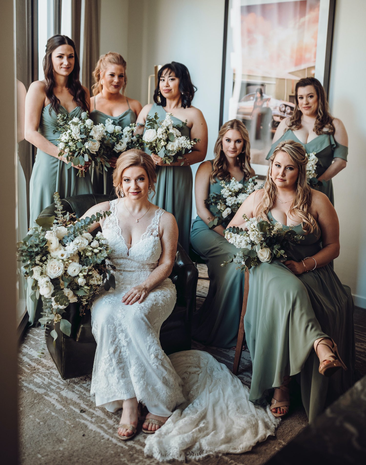 A bride smiles with her bridesmaids who wear sage green dresses for a modern music hall wedding in Houston, TX.