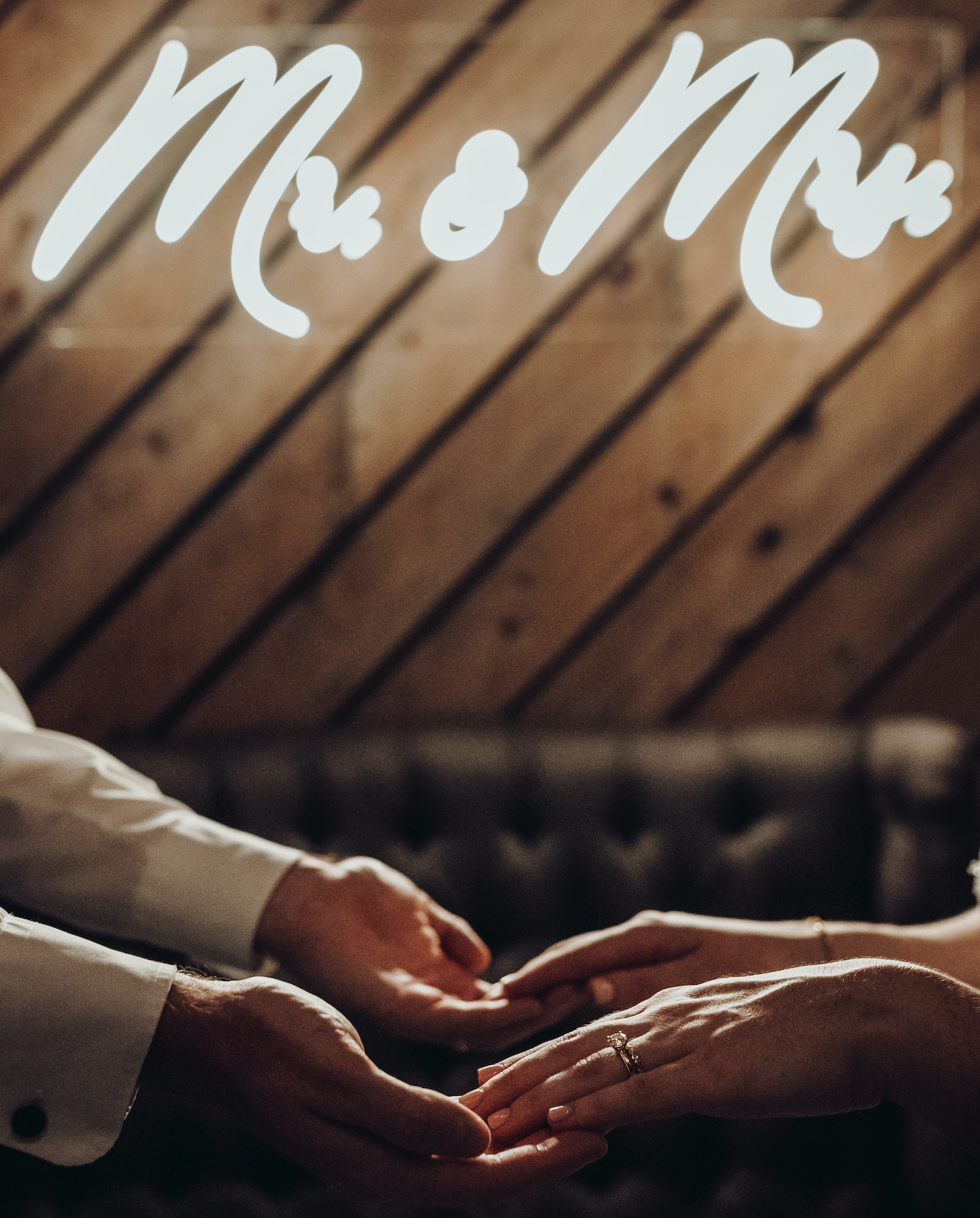 A bride and grooms hand touch in front of a neon sign that says Mr & Mrs