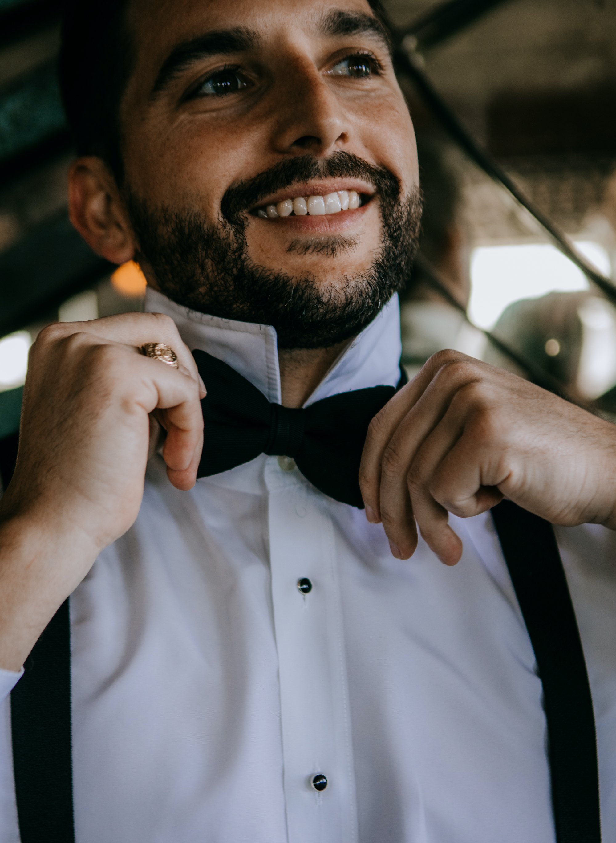 A groom is putting on his bow tie before his wedding ceremony in Houston, TX.