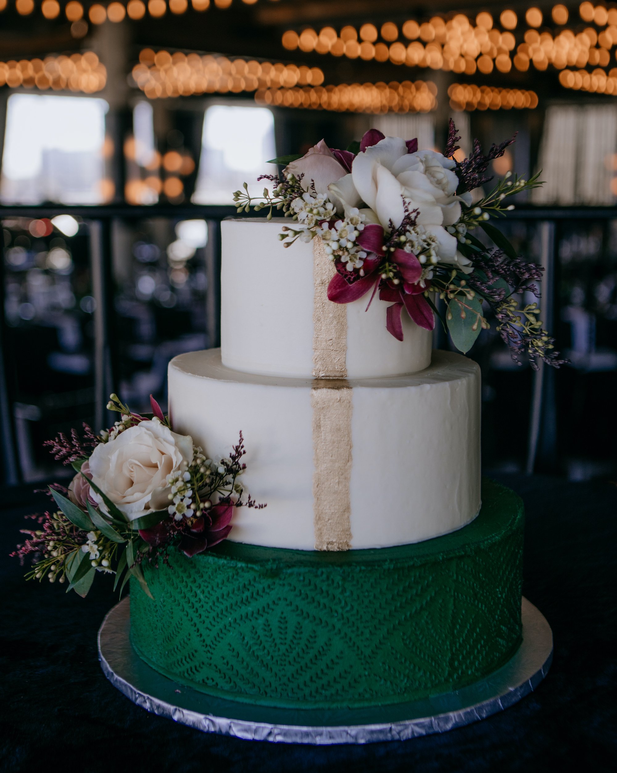 A three-tier cake with emerald green and gold accents for a Jewel Toned Wedding With Art Deco Vibes.