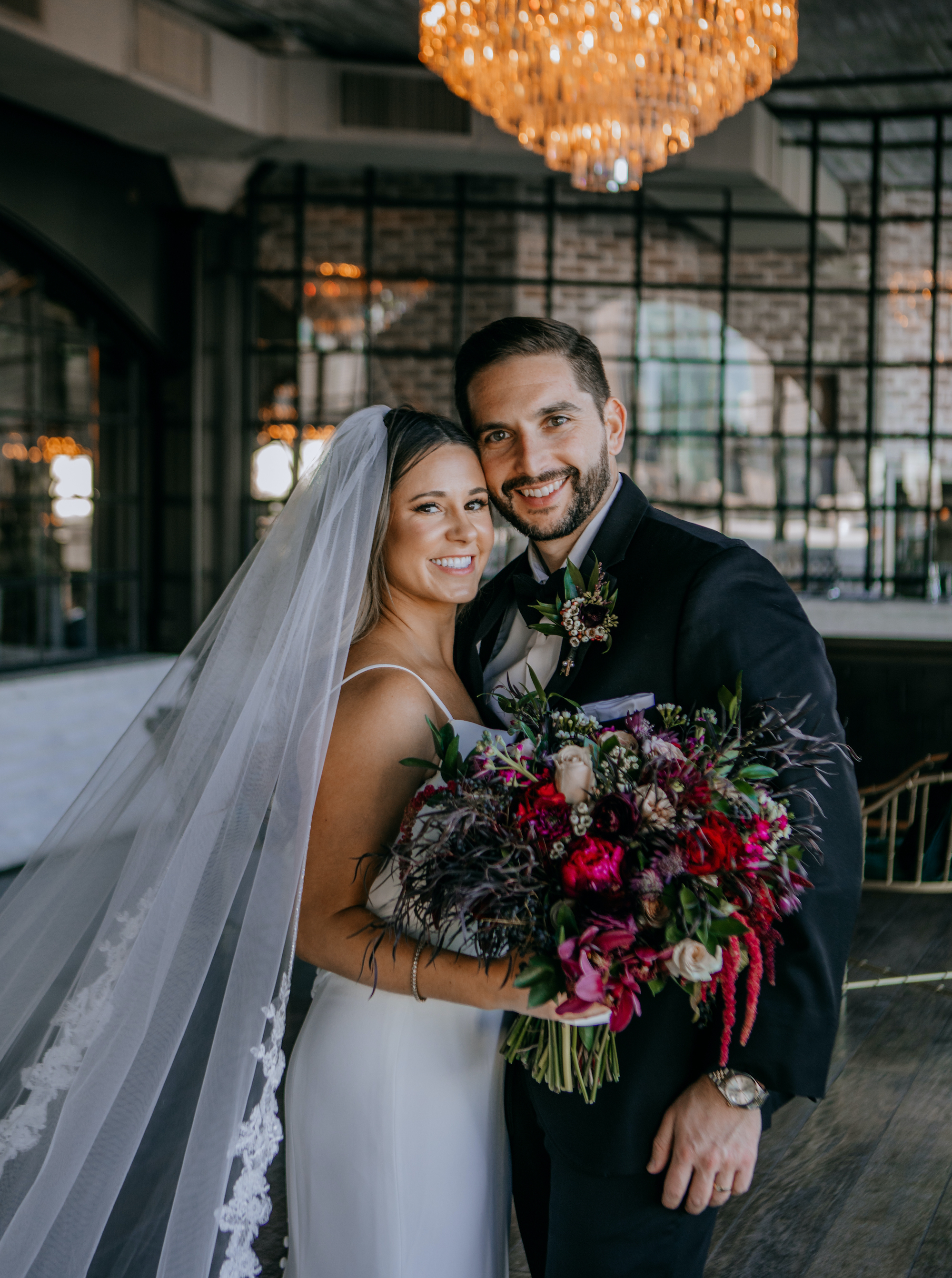A bride and groom smile together while the bride holds her jewel-toned bridal bouquet at a Houston wedding venue.