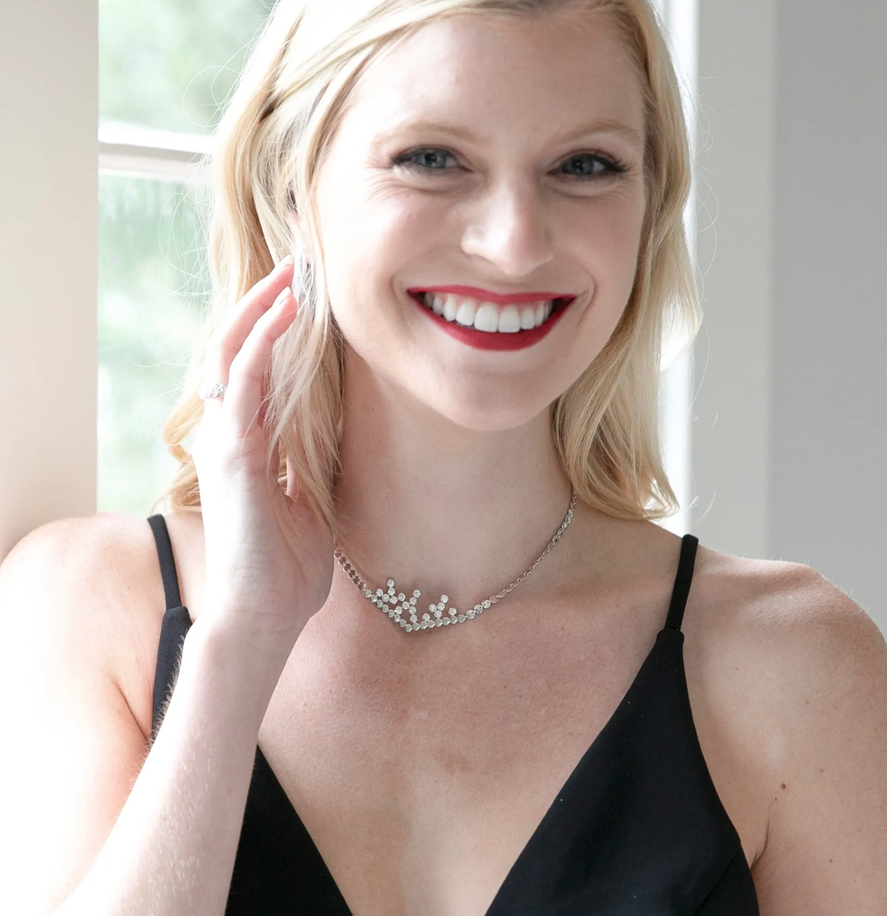 A blonde girl with red lipstick smiles and is wearing a silver necklace designed by Erin Flynn Fine Jewelry.
