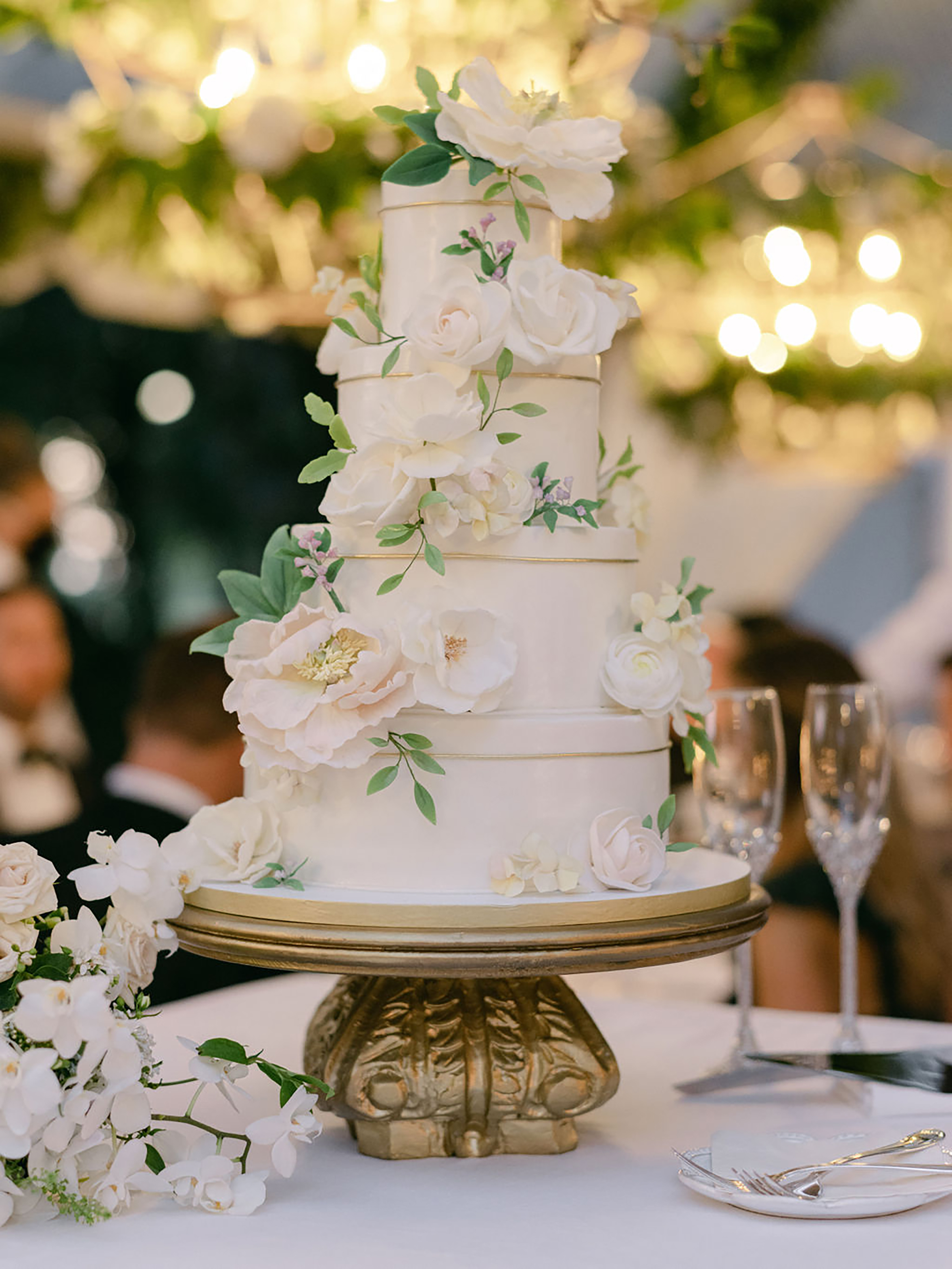 A four-tier white wedding cake with white sugar flowers artfully places on each tier.