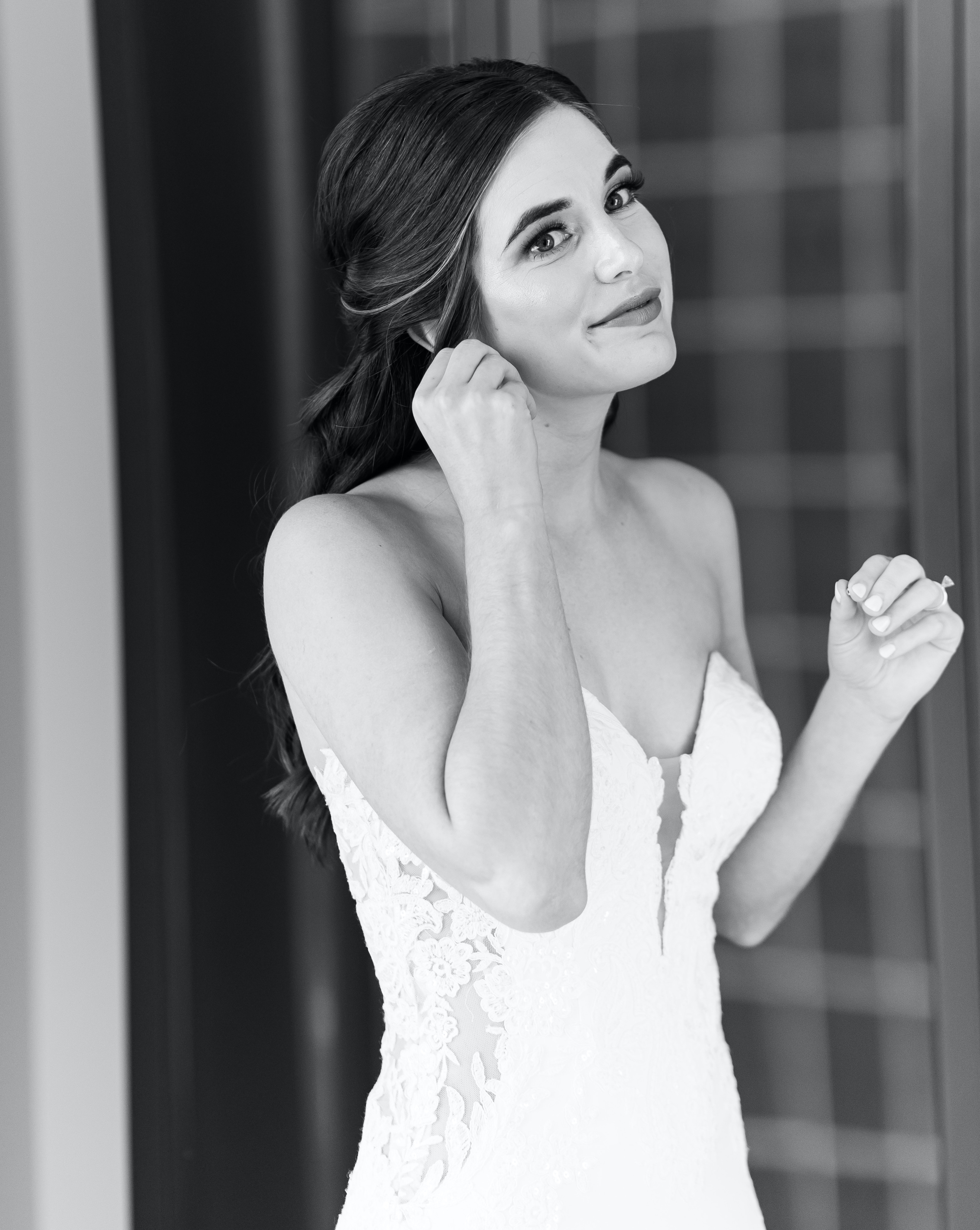 A black and white photo of a bride putting on her earring before her airy blush and sage wedding in Houston.