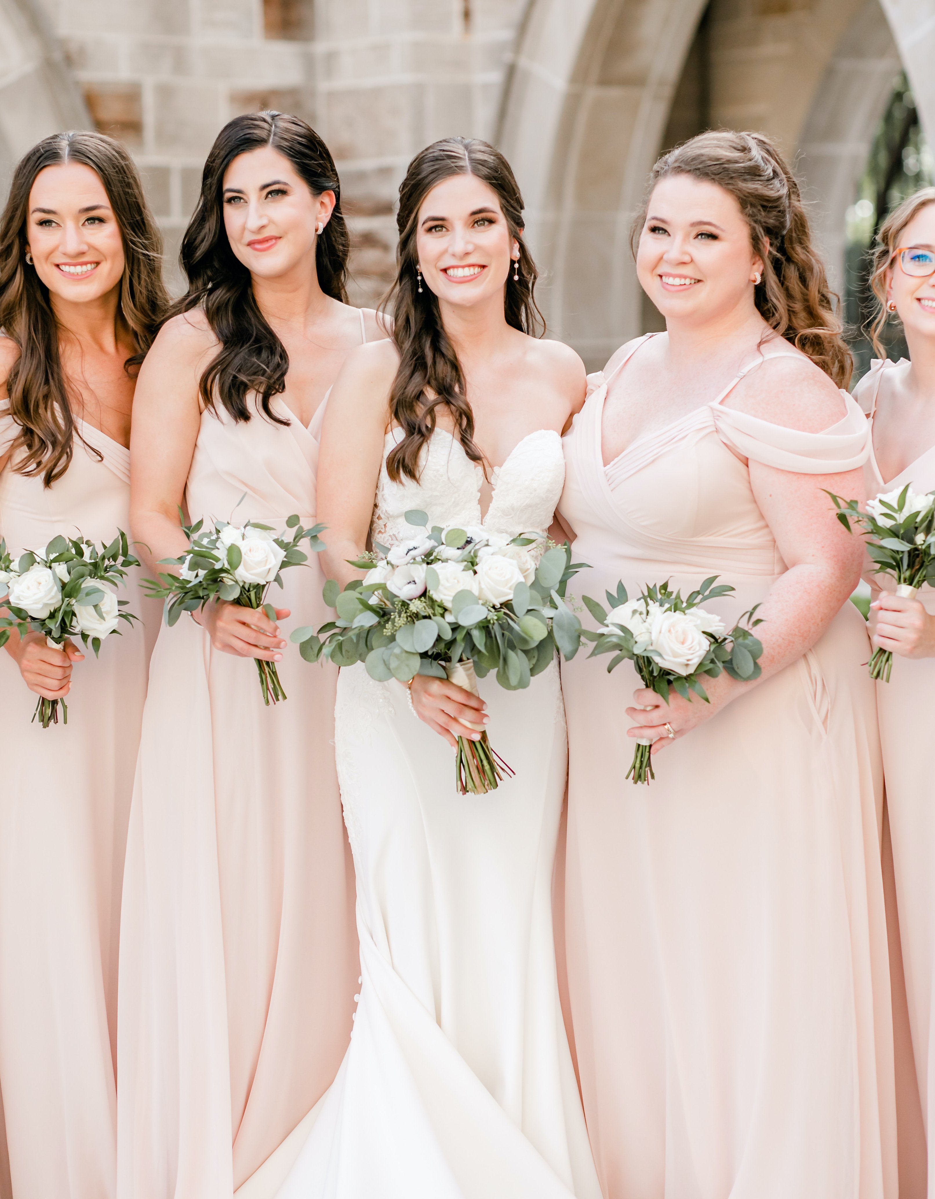 A bride stands in the middle of her bridesmaids who are wearing blush dresses.