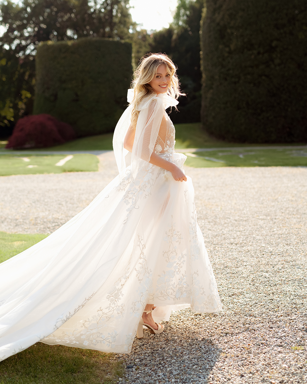A bride runs in a Berta wedding dress that has bow tie sleeves and embellished flowers.
