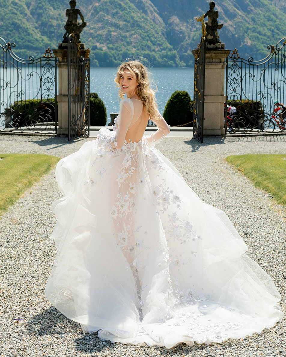 A bride runs towards Lake Como in Italy in a flowy wedding dress with embellished flowers.