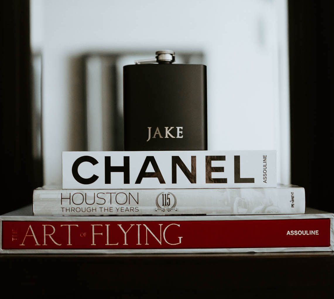 A flask engraved with the groom's name sits on tops of several coffee table books including Chanel, Houston Through the Years and The Art of Flying.