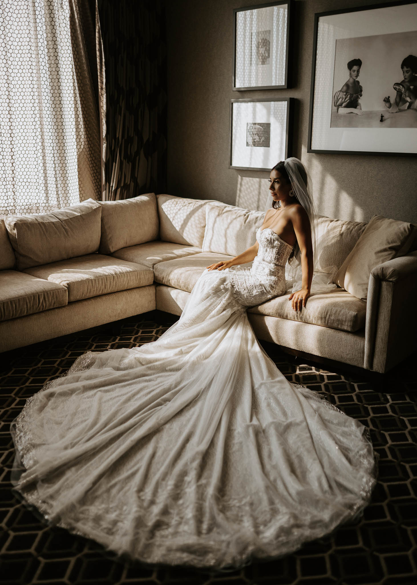 A bride sits on a couch with her wedding dress skirt spread around her. She looks out the window before her earth-toned wedding at The Bell Tower on 34th in Houston, TX.