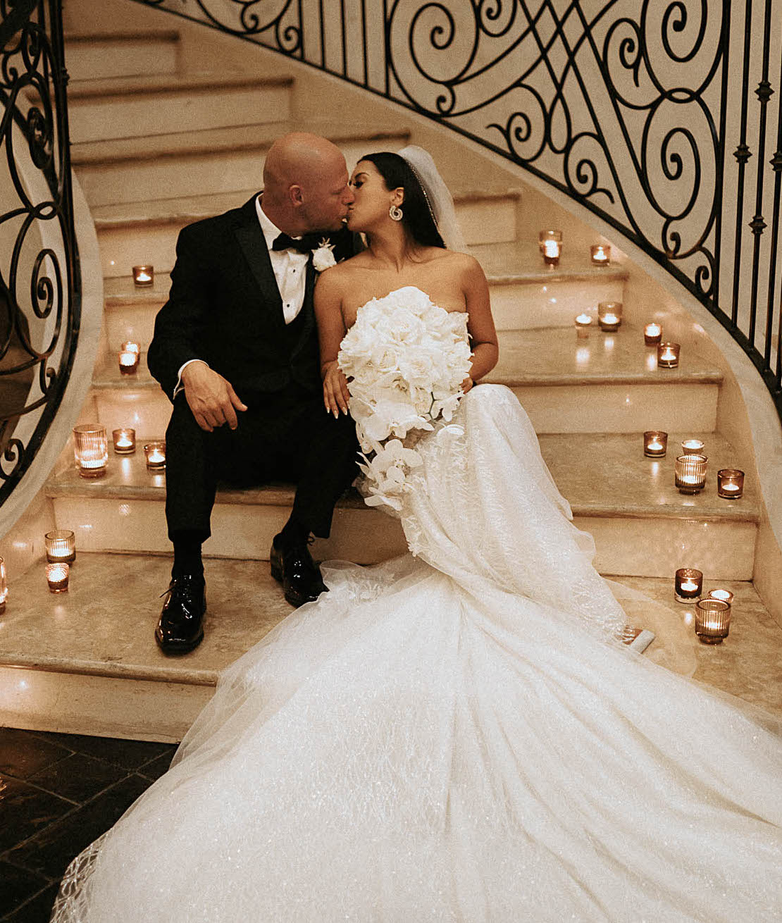 A bride and groom kiss on a staircase with lit candles surrounding them on the steps at The Bell Tower on 34th in Houston, TX.