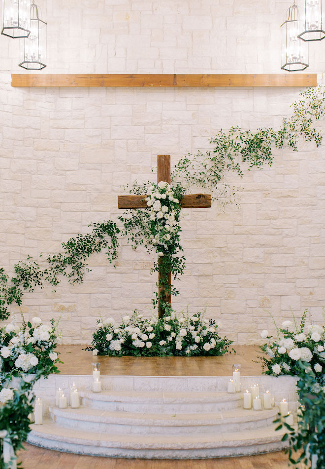 A limestone chapel with a wood cross decorated with white florals and greenery. 