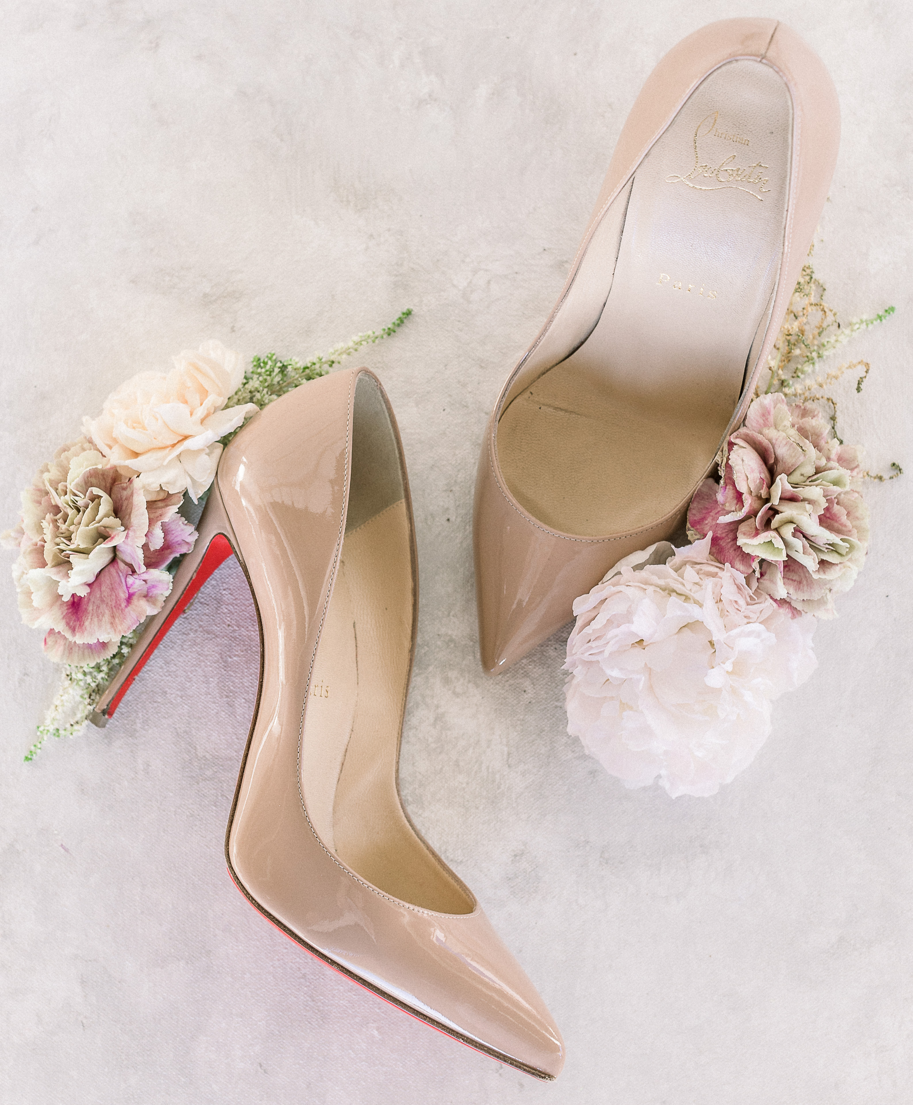 A nude pair of Christian Louboutin pumps are decorated with mauve pink and white flowers on the heels.