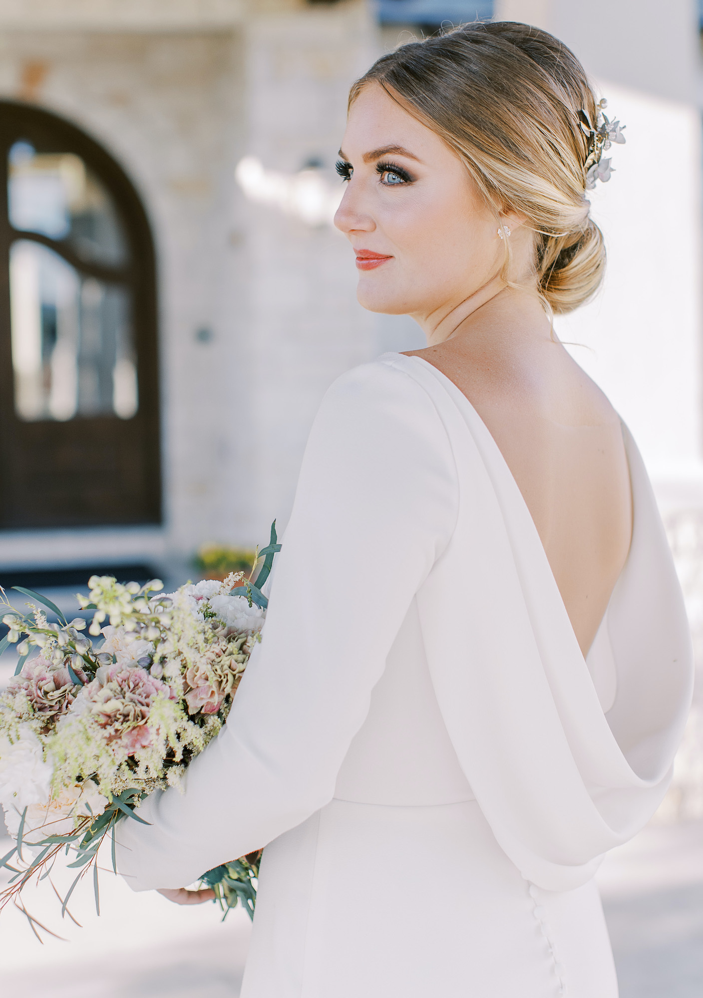 A bride holds her bridal bouquet and looks to the side so her backless wedding dress is visible.