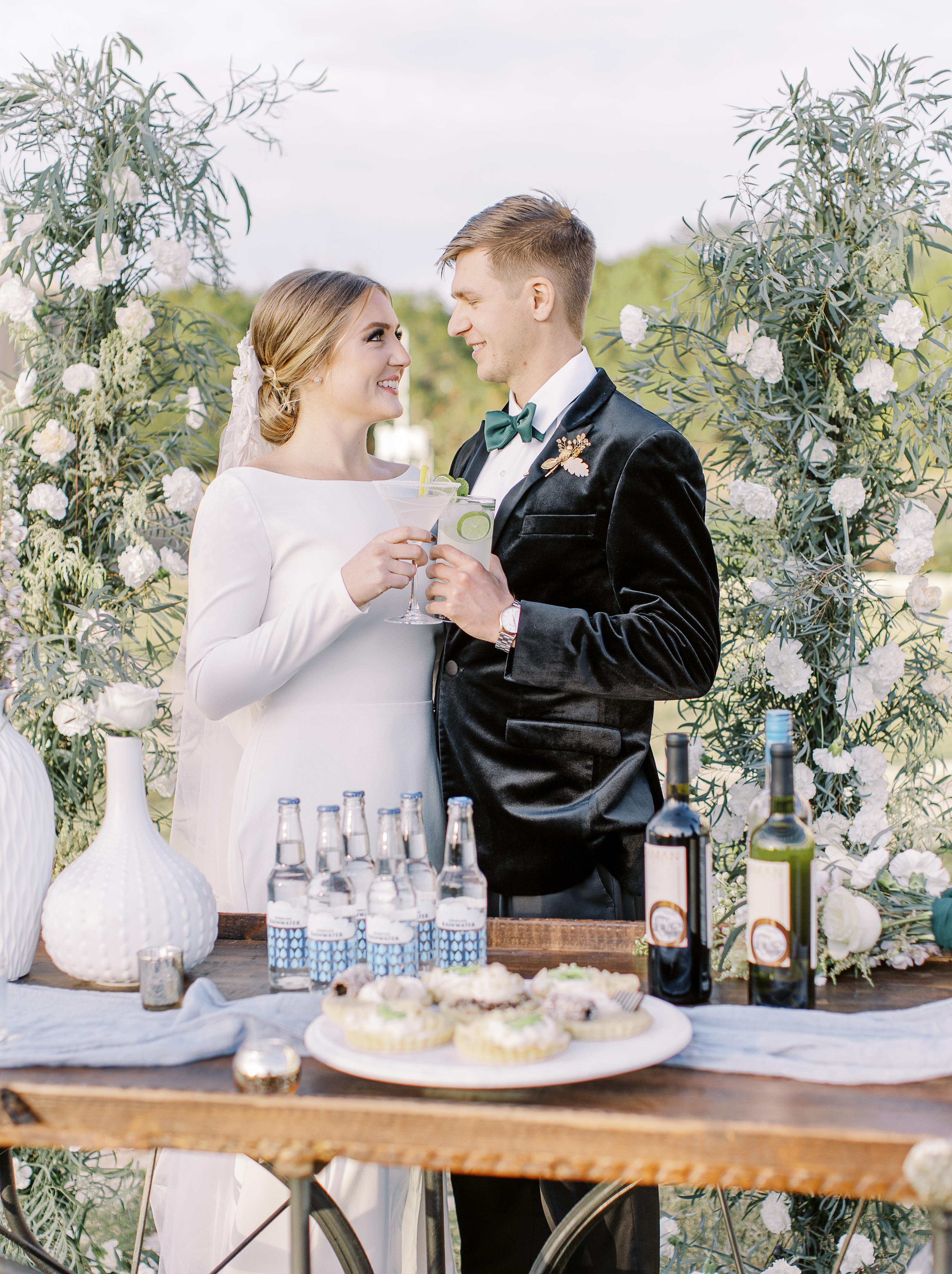 A bride and groom cheers while standing behind a vintage bar cart outside at Cricket Hill Ranch in Dripping Springs, TX.