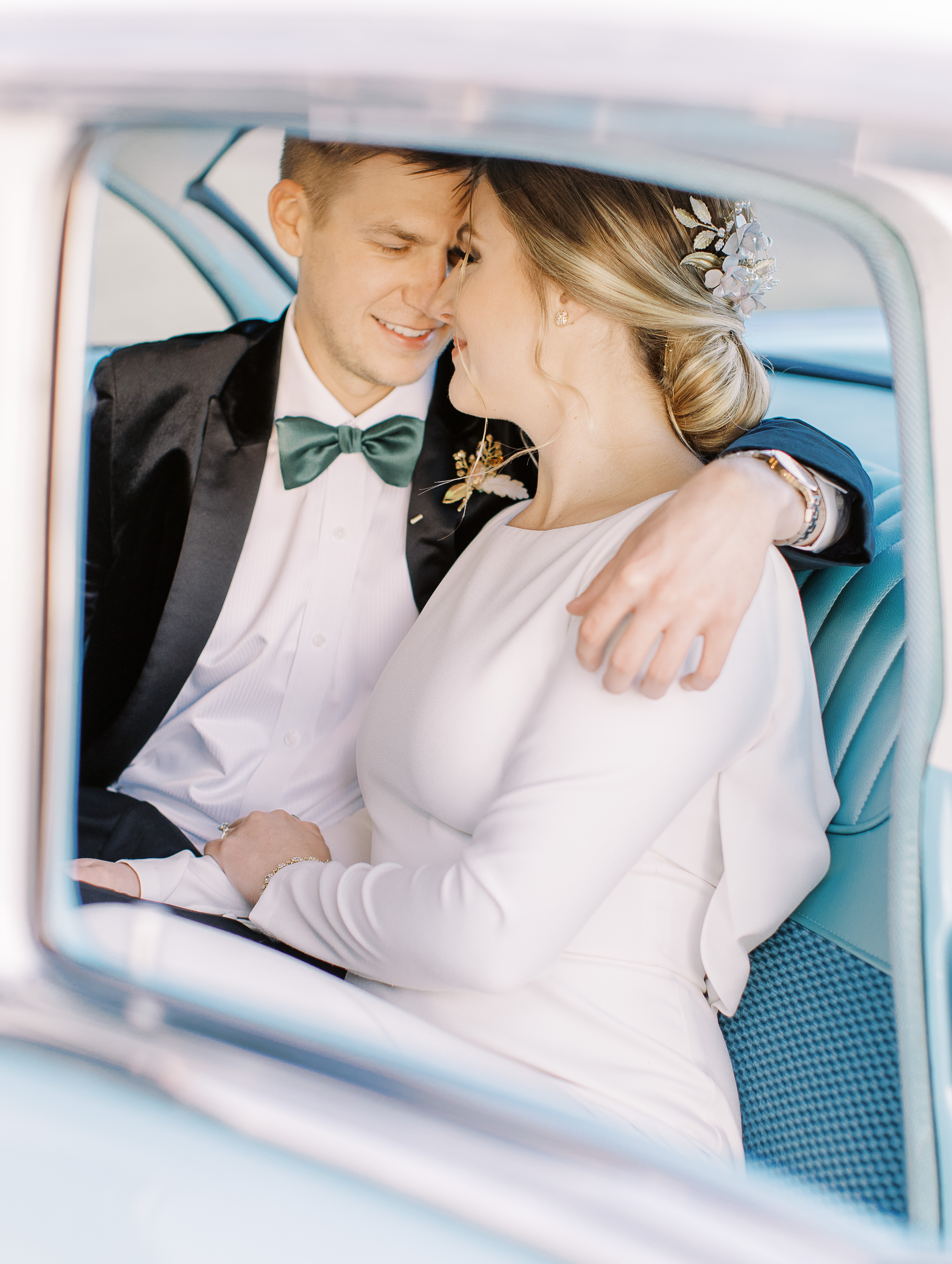 A groom puts his arm around his bride as they sit in the backseat of a vintage light blue car in Dripping Springs, TX at Cricket Hill Ranch.