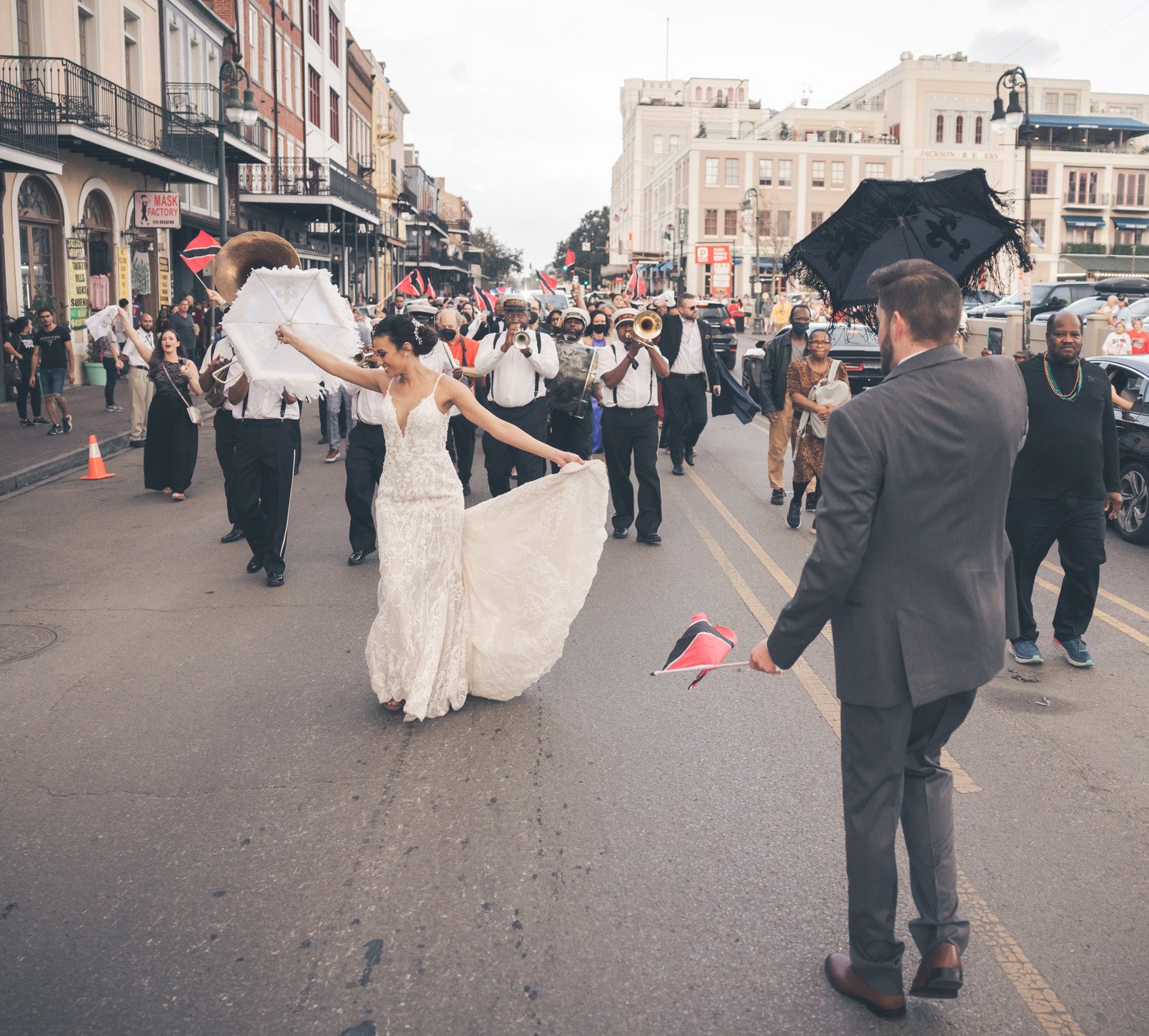 A bride and groom hold umbrellas in the air and lead a parade in the streets of New Orleans on their wedding day.