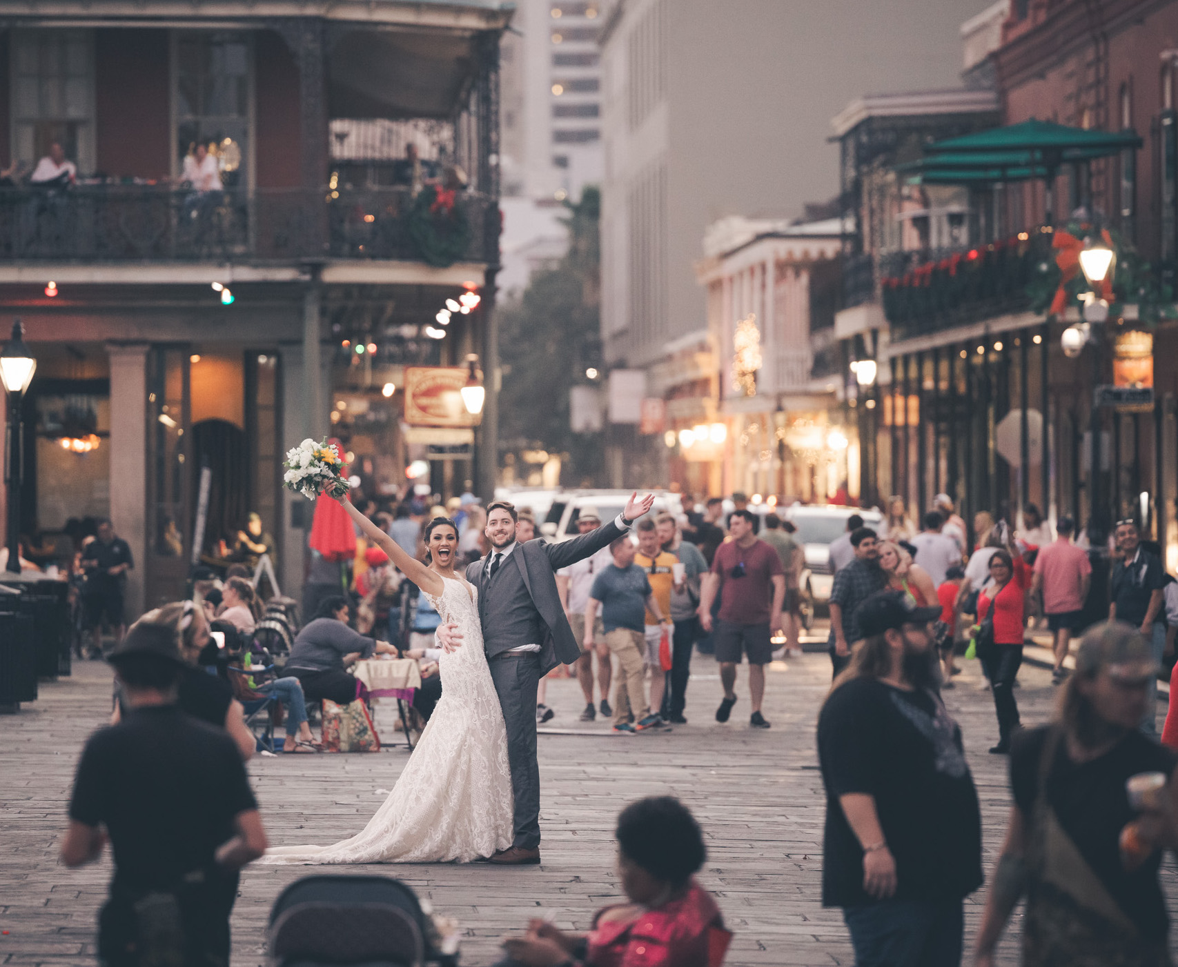 A bride and groom raise their hands in the air while standing in the middle of the French Quarter on their wedding day.