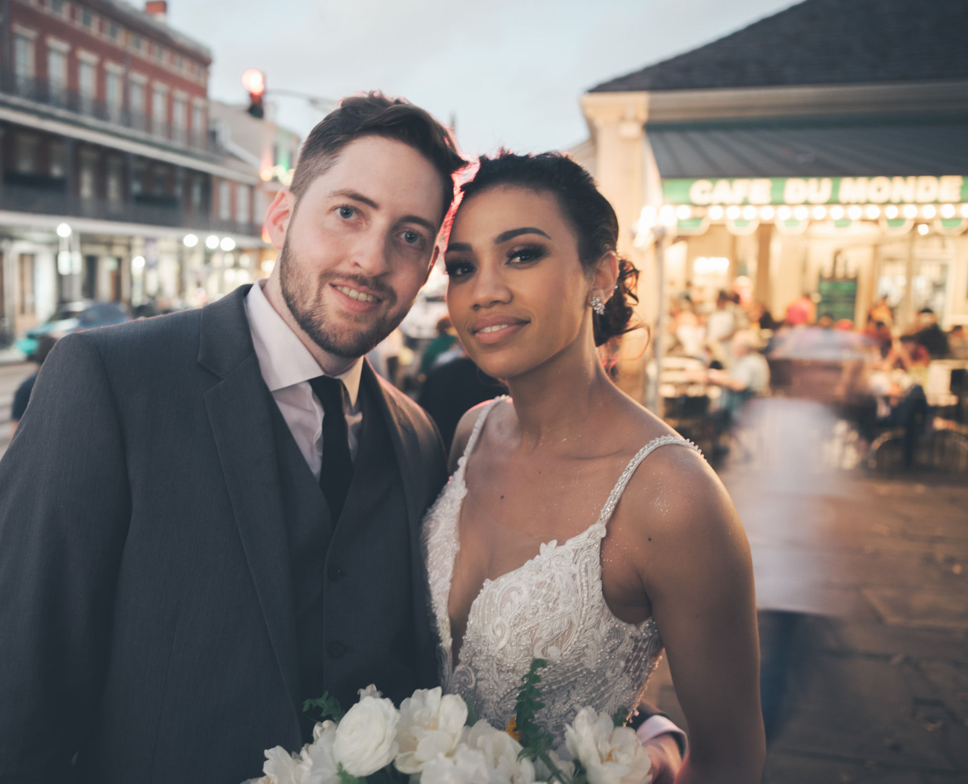 A bride and groom smile at the camera with Cafe Du Monde in the background.