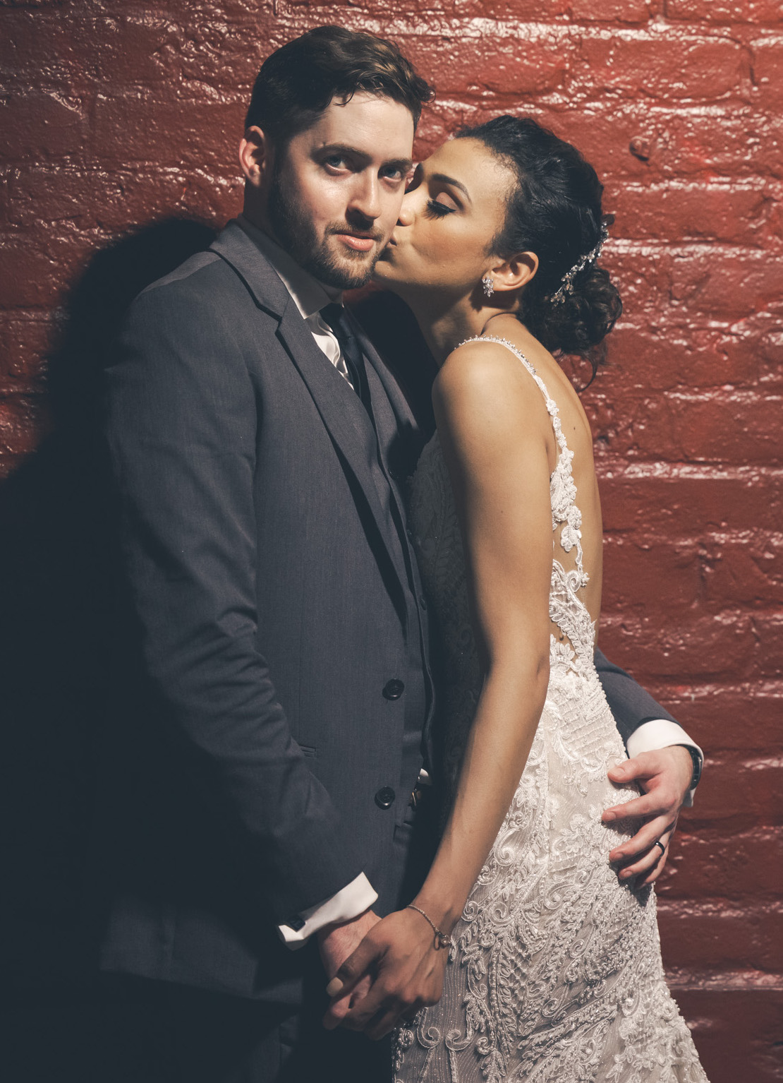 A bride and groom stand against a red brick wall in New Orleans.