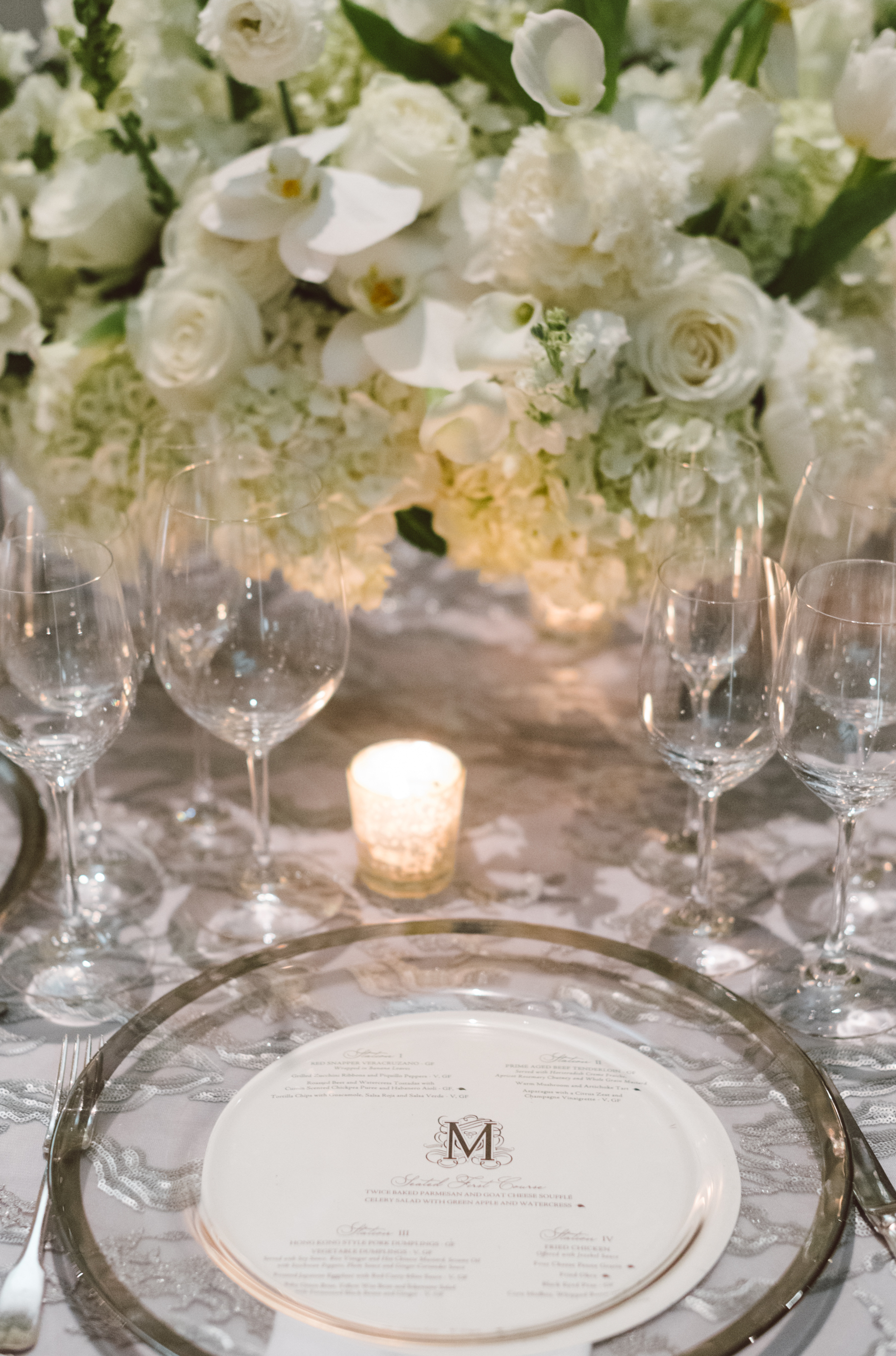 A flower centerpiece is full of white flowers and sits next to a place setting for an opulent winter wedding in Houston, TX.