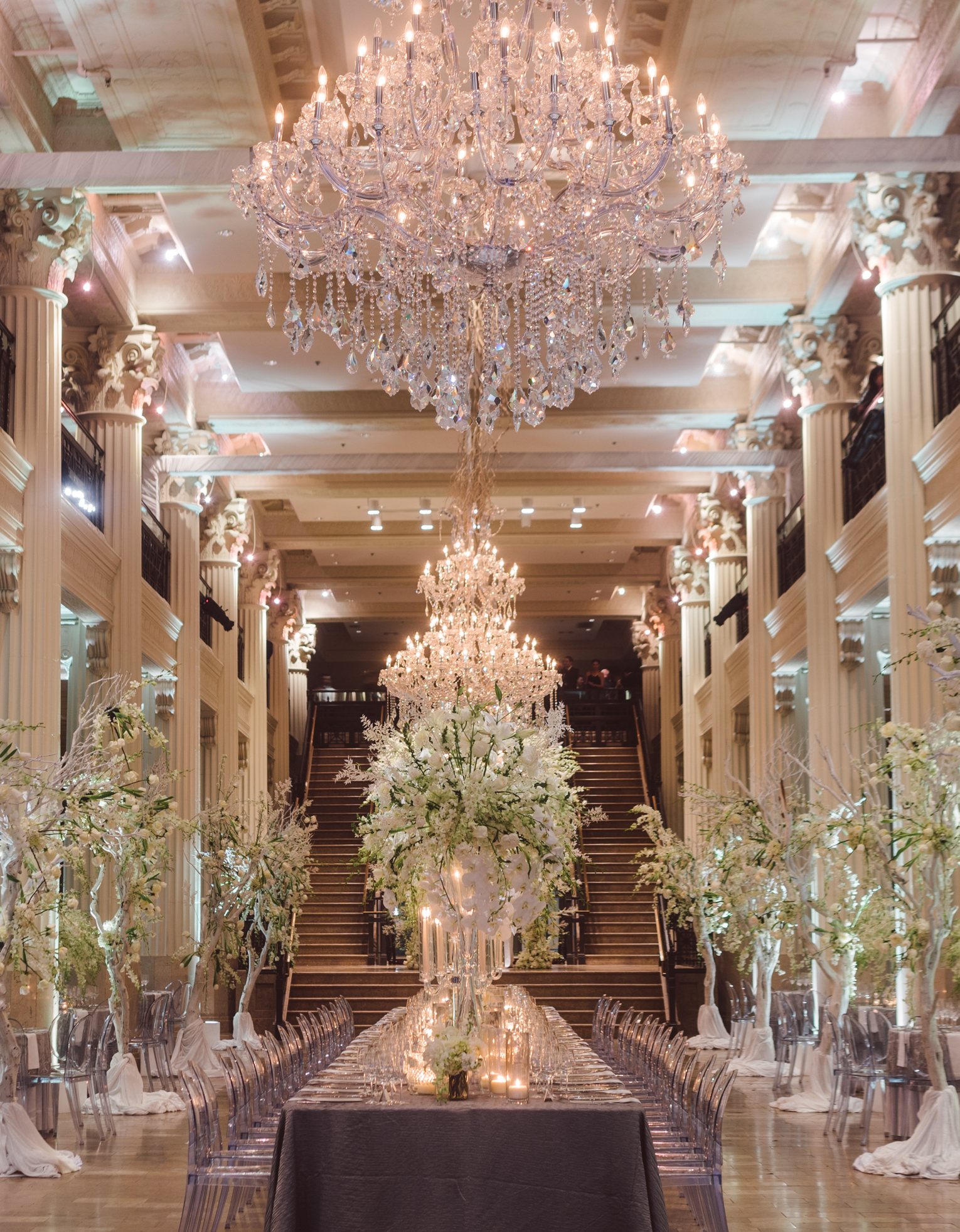 A reception space at Corinthian Houston is decorated with crystal chandeliers and white flower installations surrounding the tall and spacious room.