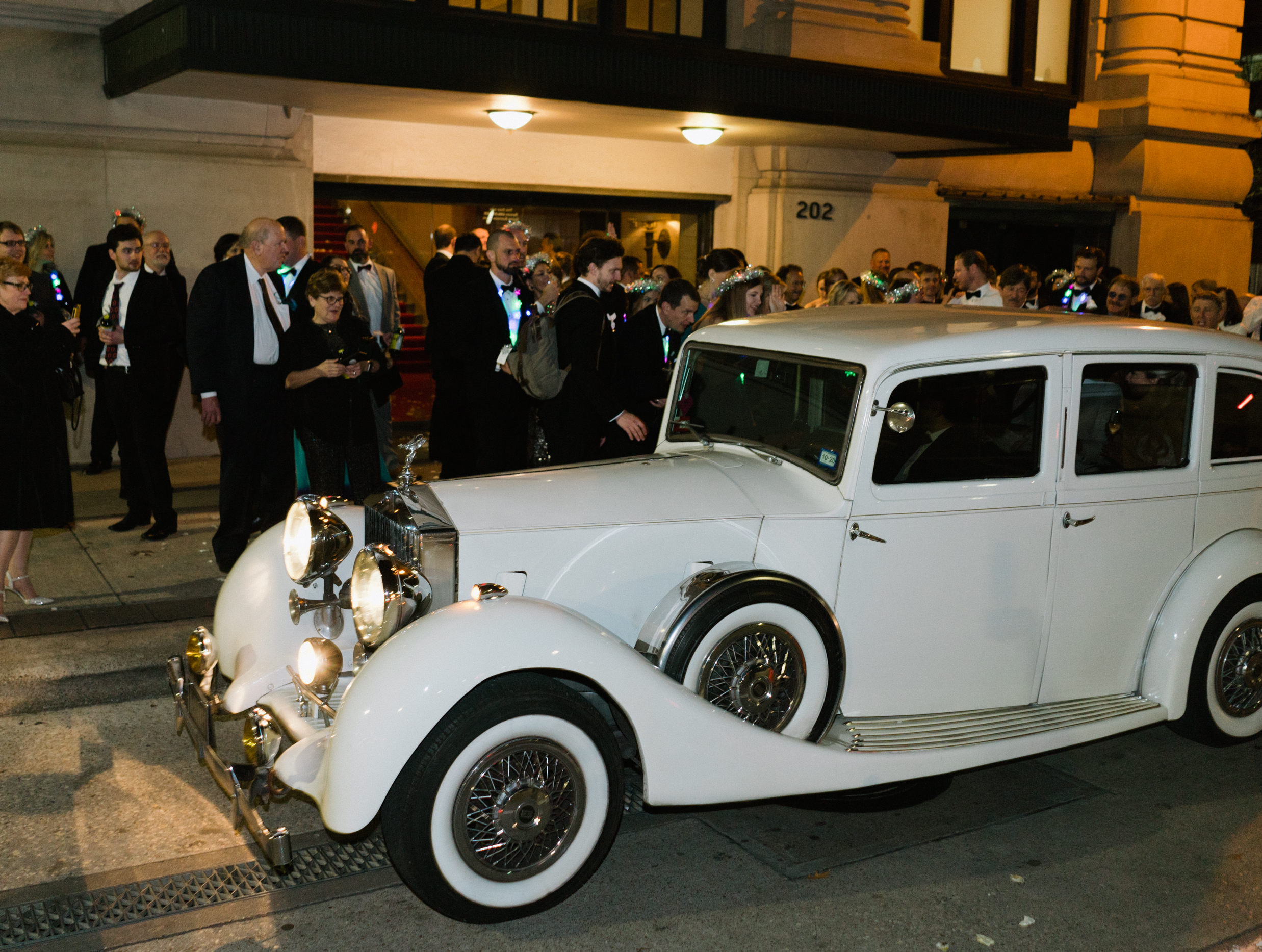 A white vintage car is parked outside of a wedding venue in Houston for a bride and groom to get inside.