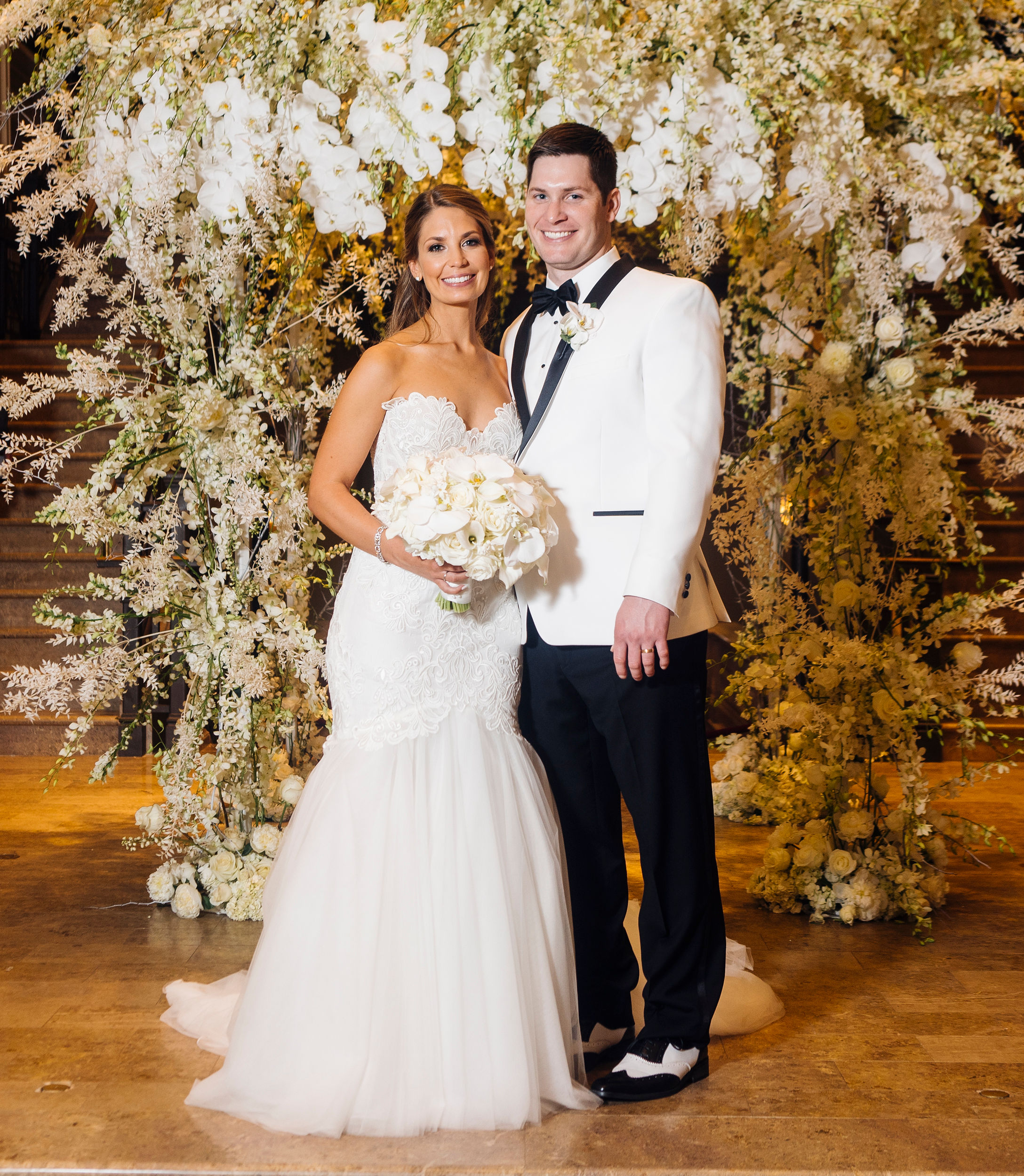 A bride and groom stand in front of a flower installation for their opulent winter wedding.