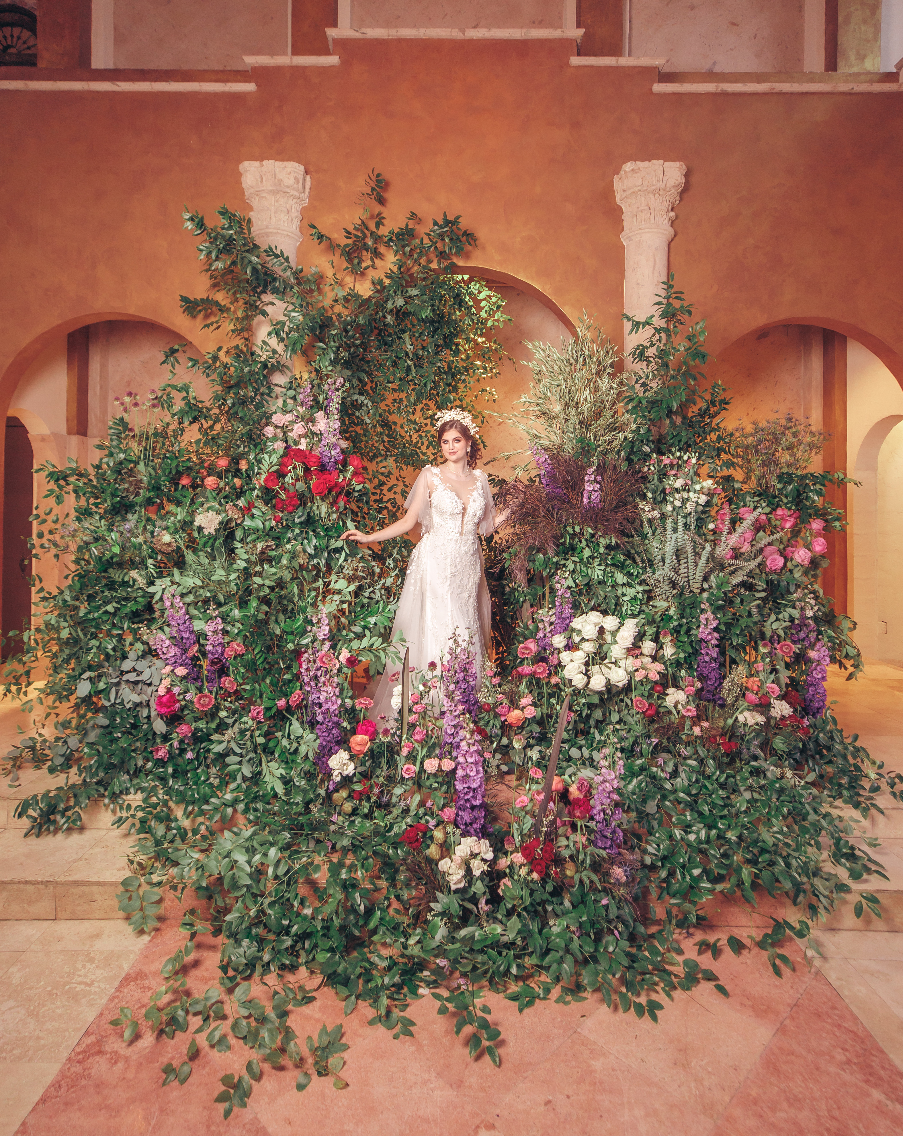 A bride stands in the middle of greenery and colorful flowers in the chapel at The Bell Tower on 34th.