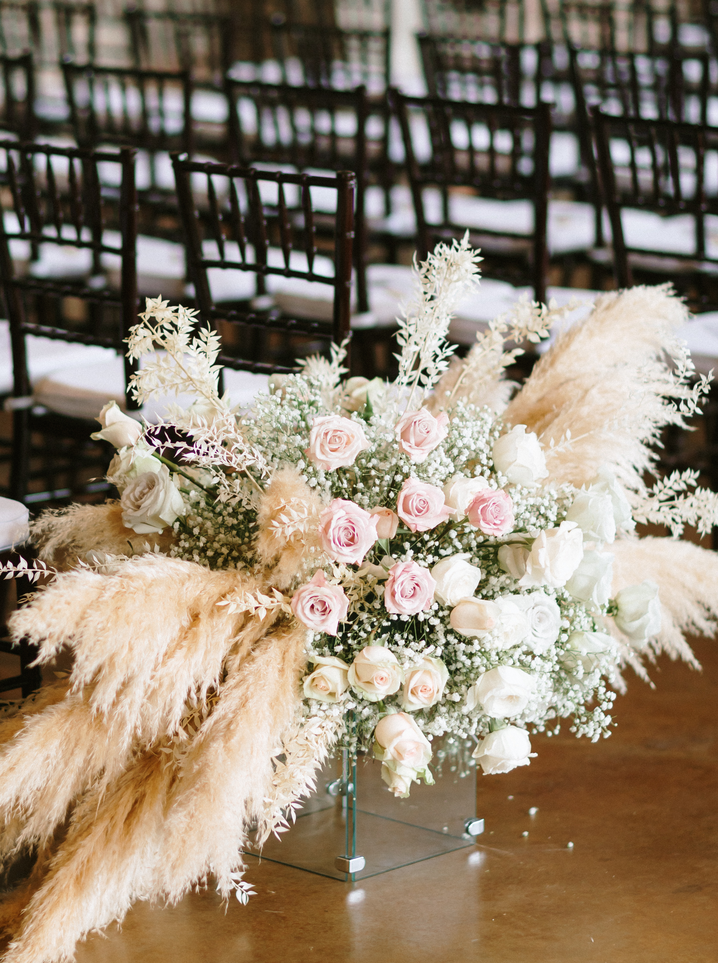 A flower arrangement full of blush pink flowers and pampas grass is set up in one of the aisles for a wedding ceremony in Montgomery, TX.