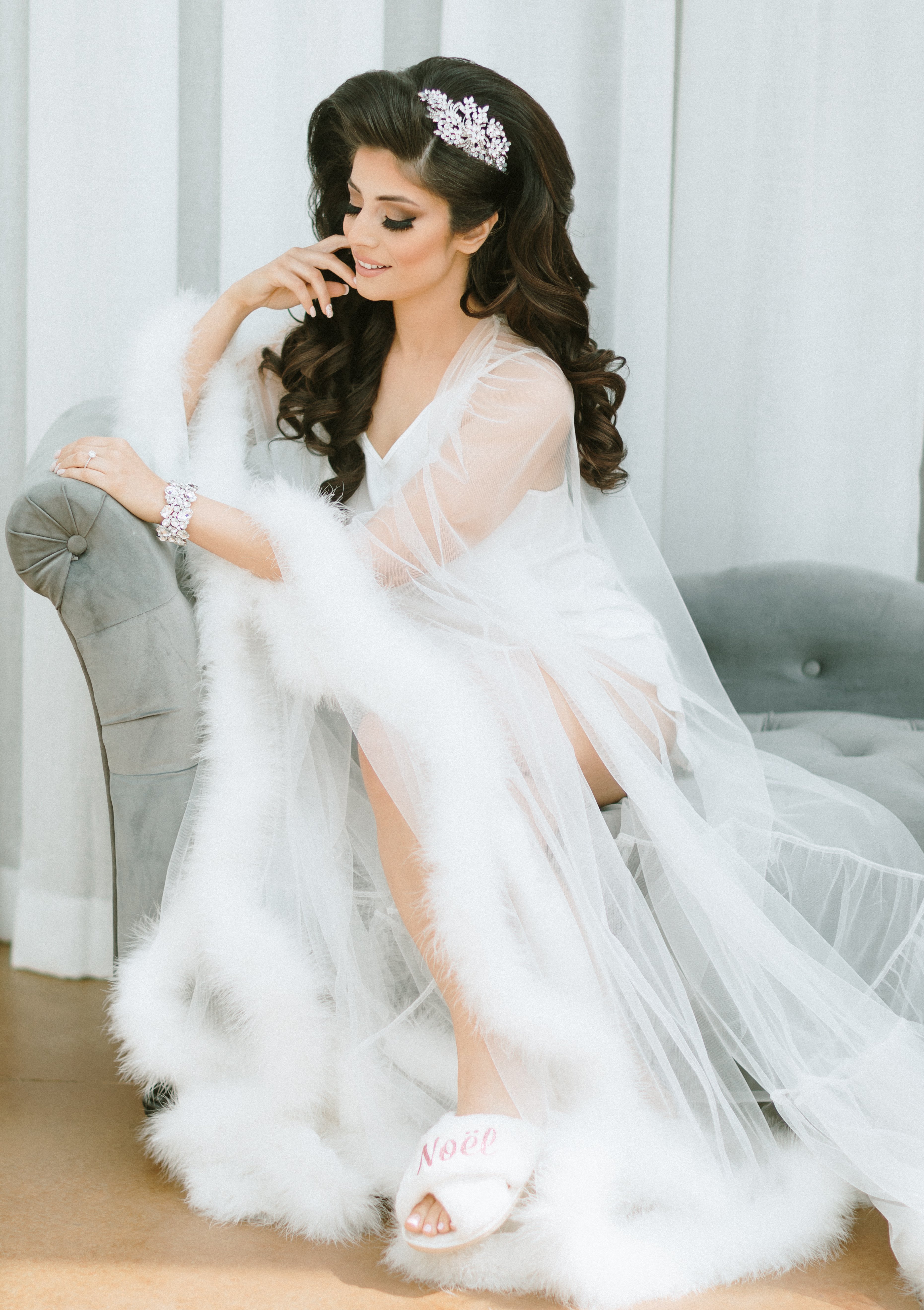 A bride wears a sheer robe with feathery accents on the ends of it before her pink and lilac Persian wedding.