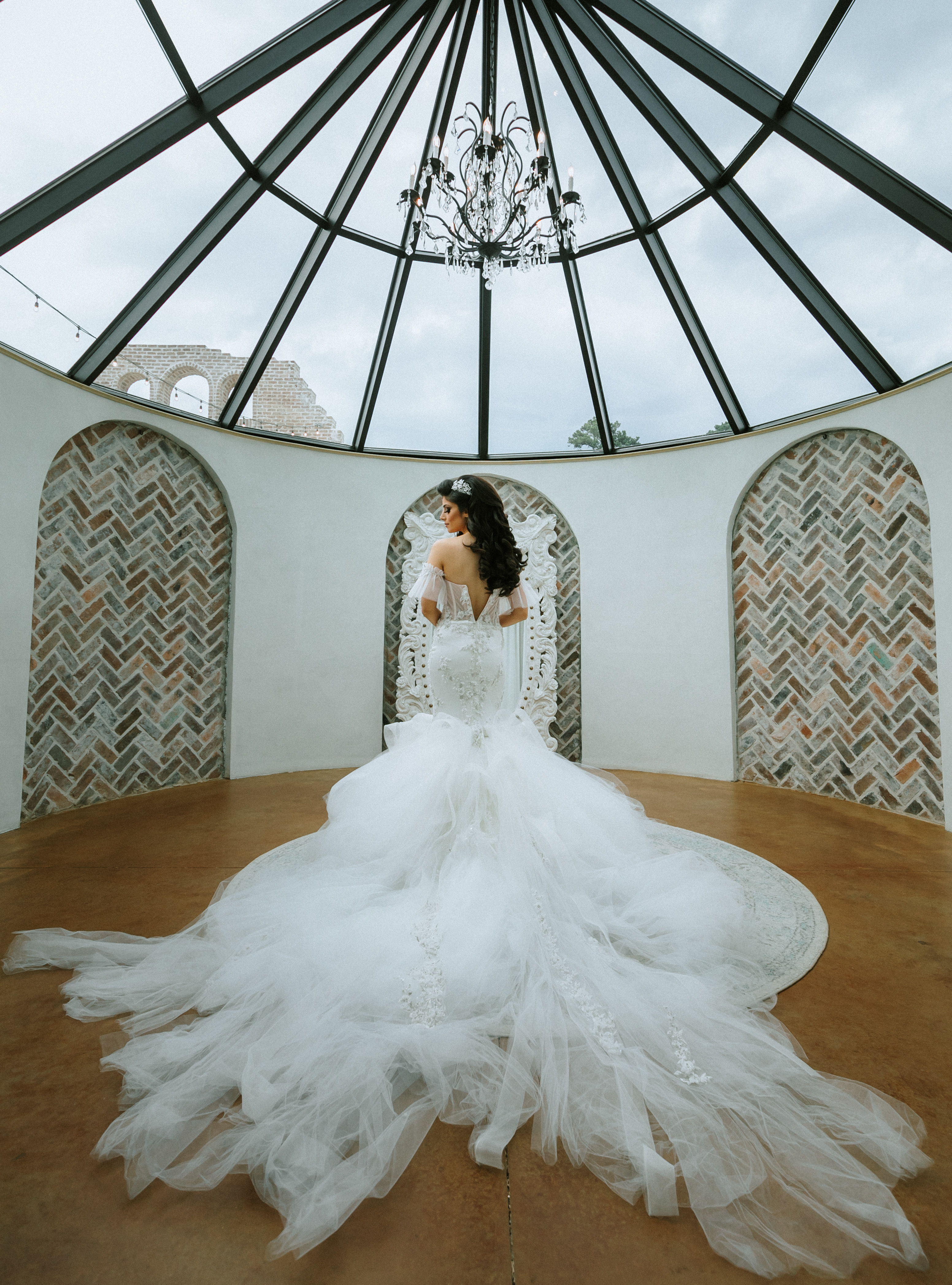 A bride stands in the bridal suite in her wedding dress that has a trailing veil.