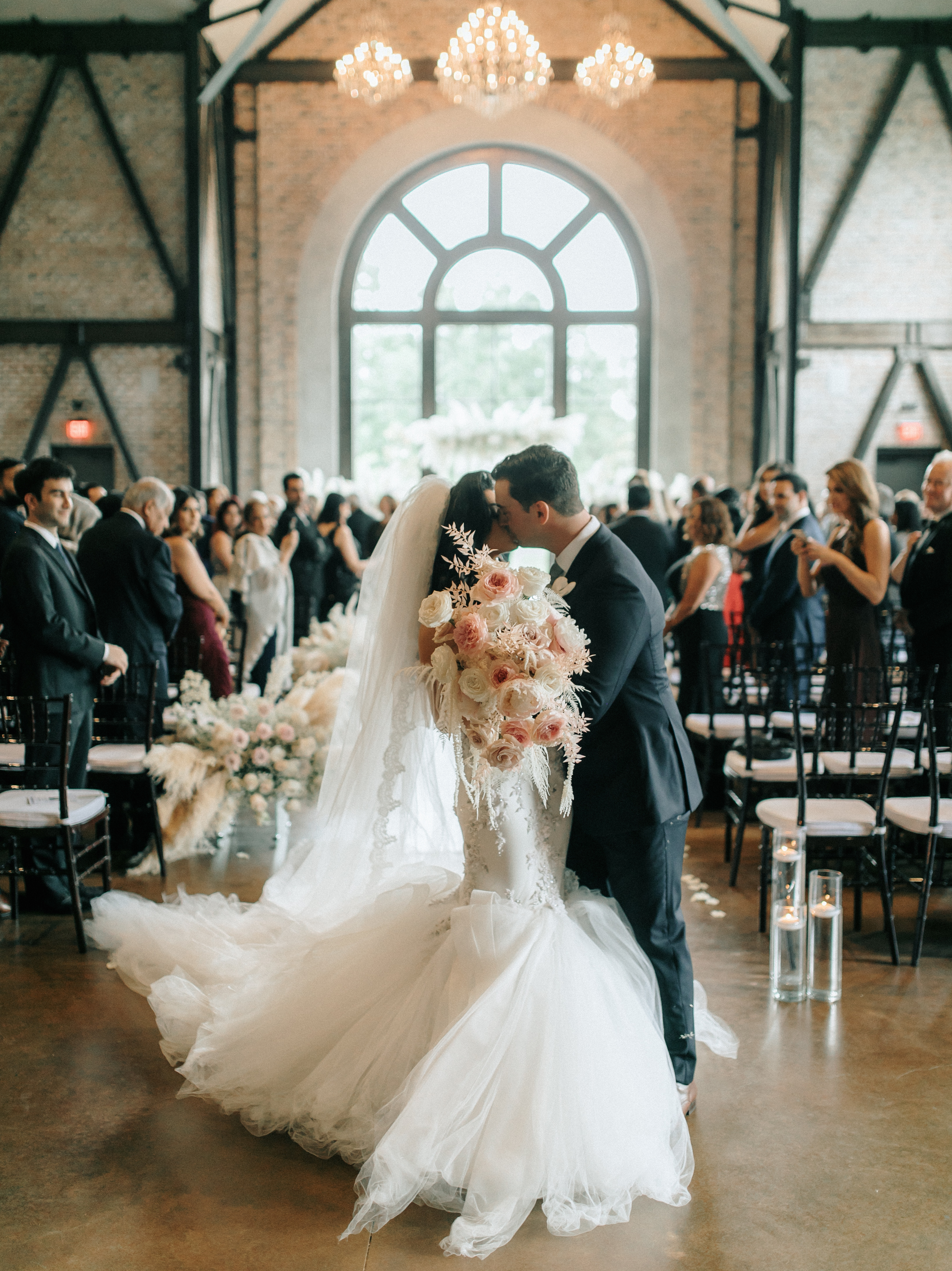 A bride and groom kiss in the middle of the aisle during their pink and lilac Persian wedding.