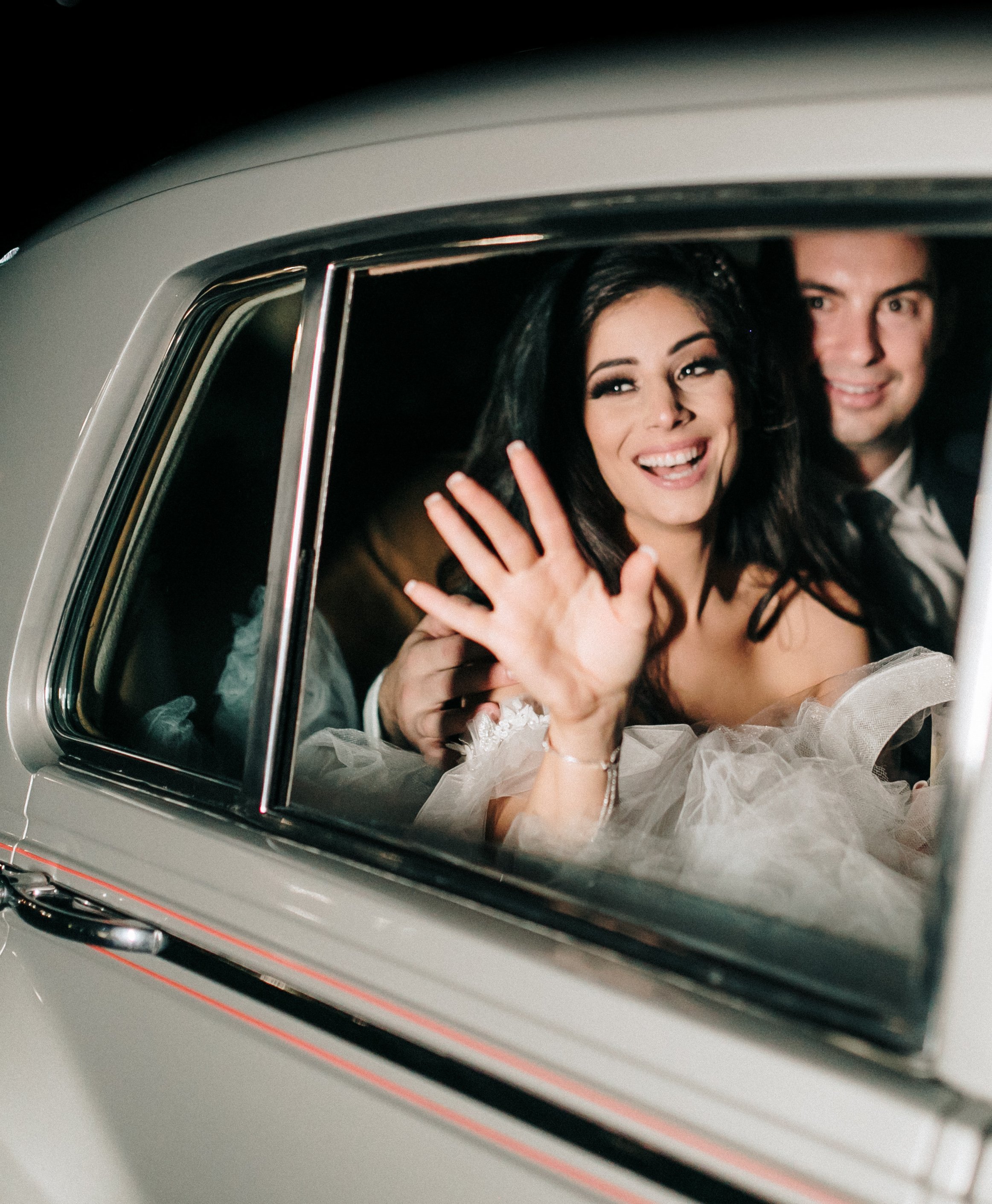 A bride and groom sit in the back seat of a car and wave to their wedding guests as they leave their wedding reception in Montgomery, TX.