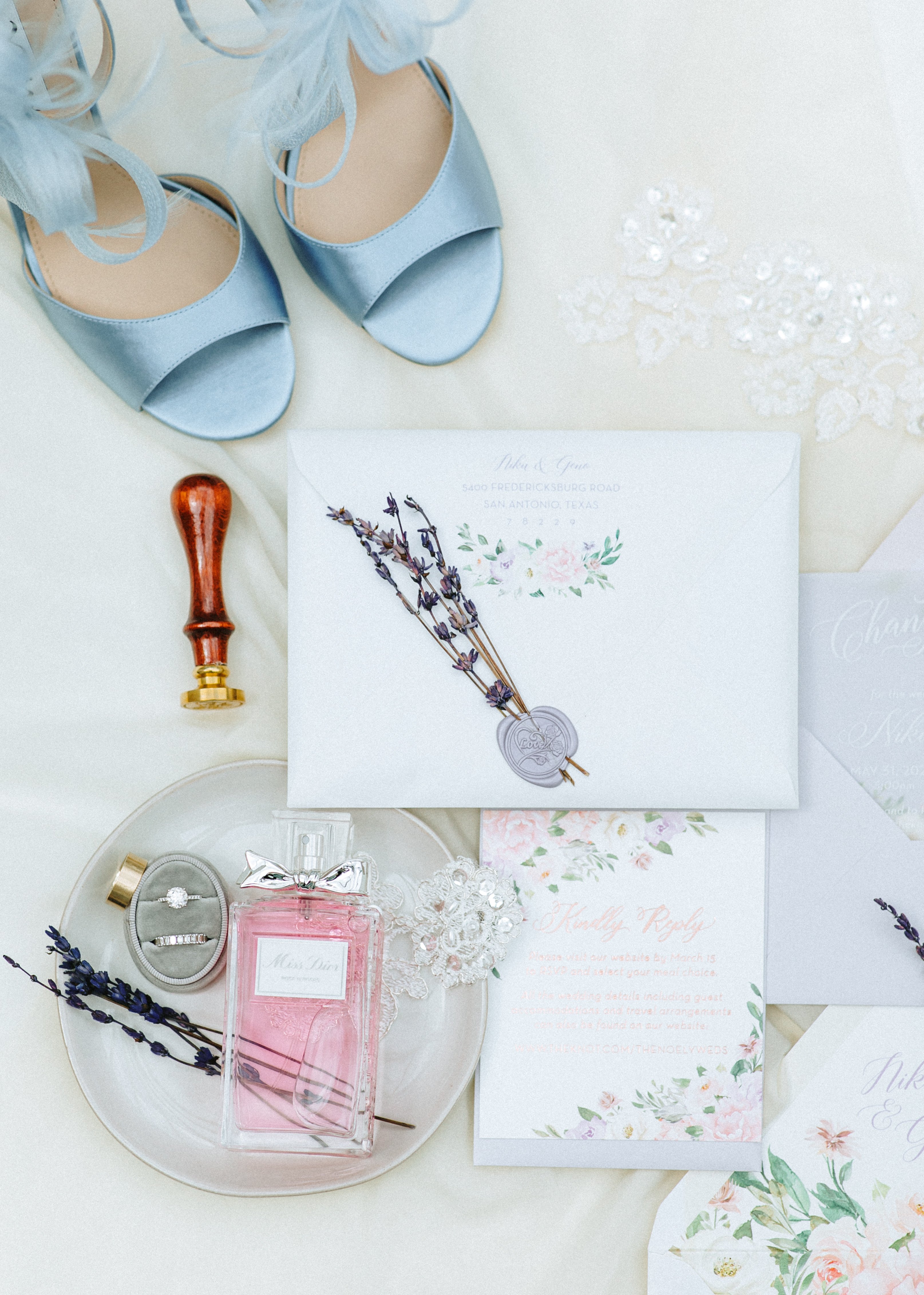A flatlay with lilac invitations and light blue shoes for a pink and lilac Persian wedding in Montgomery, TX.