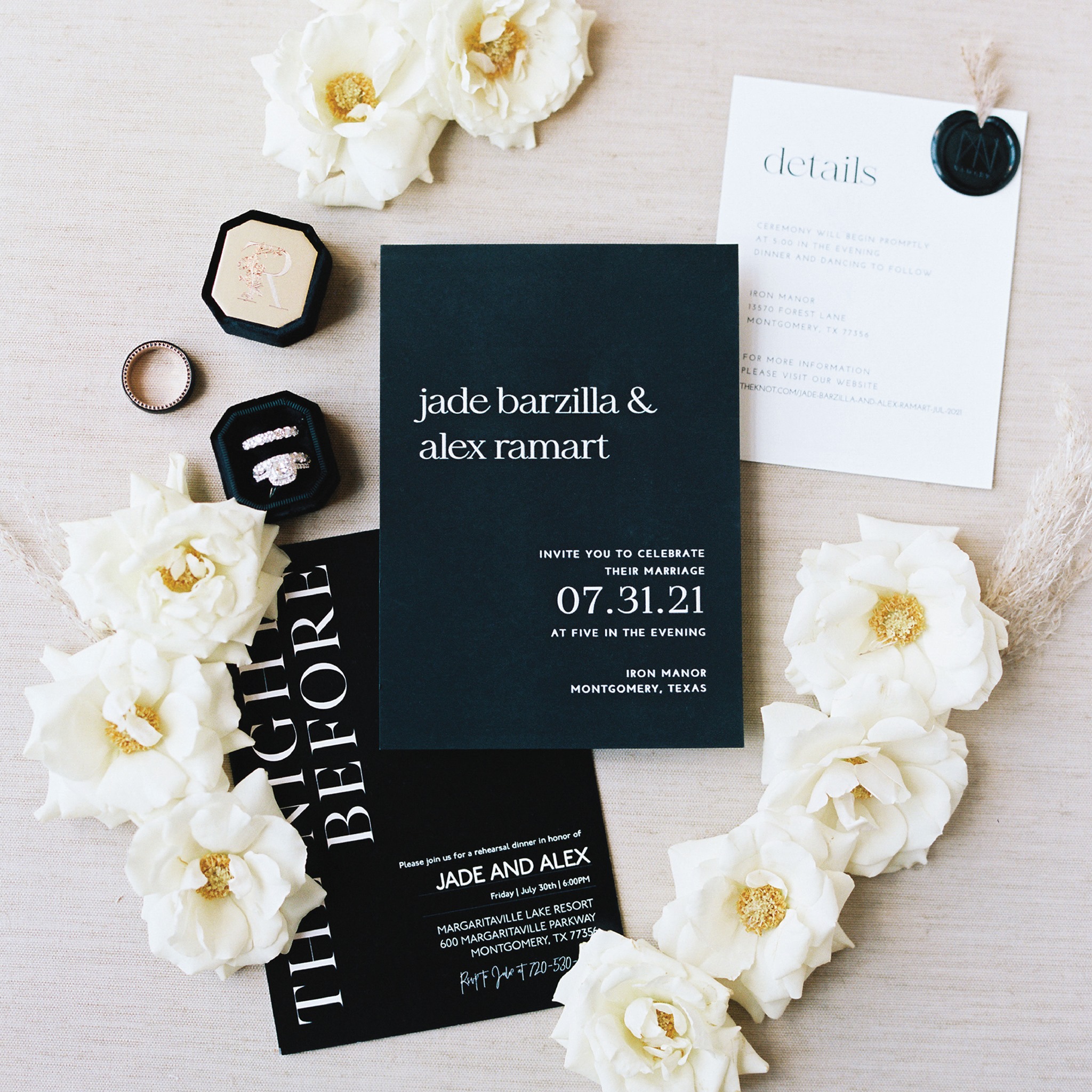 A black, navy and cream invitation suite for a wedding surrounded by fresh roses and a velvet box with an engagement ring.