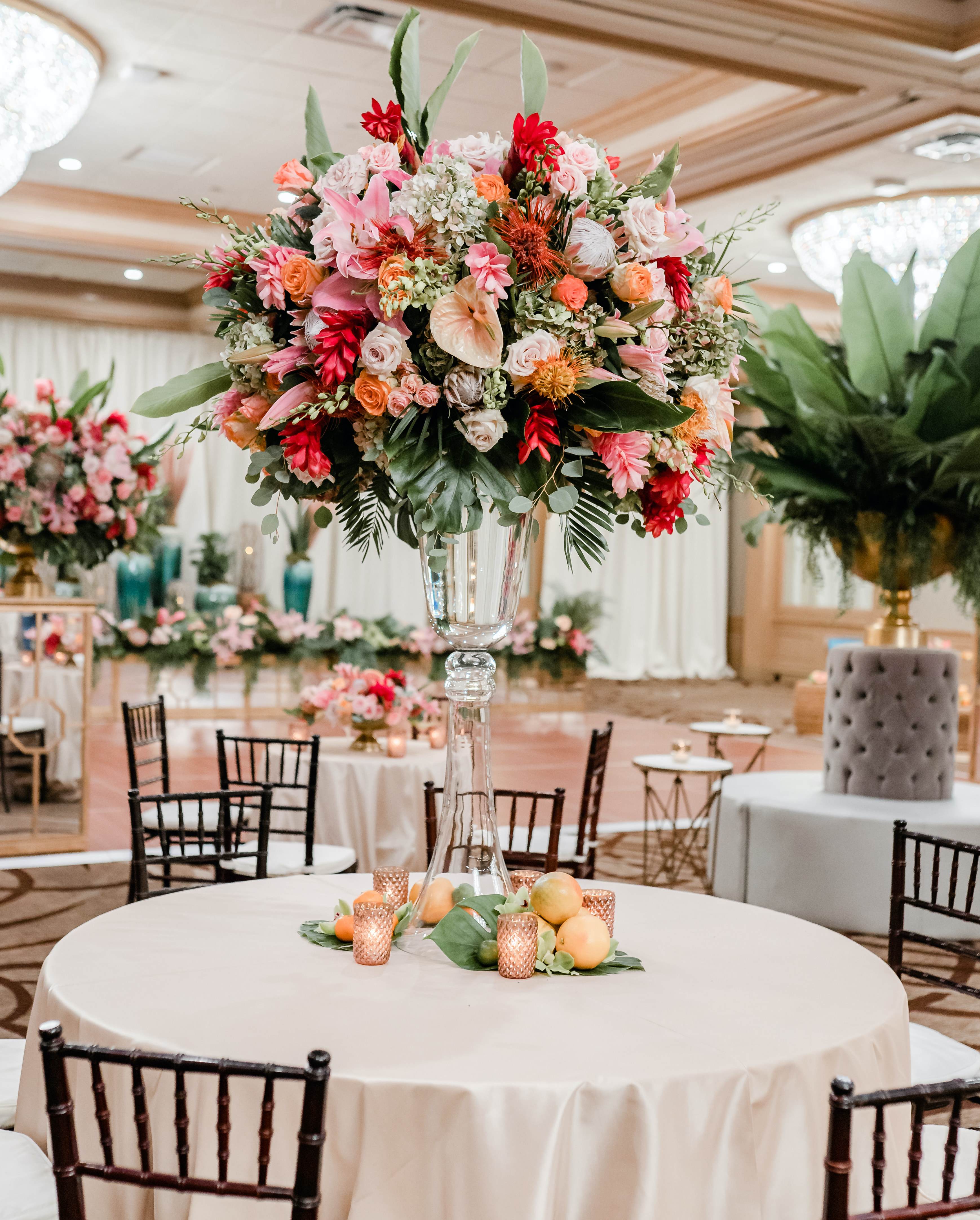 A tall centerpiece full of tropical orange, pink and red flowers sits on a table for a tropical wedding reception in the ballroom at The San Luis Resort, Spa & Conference Center.