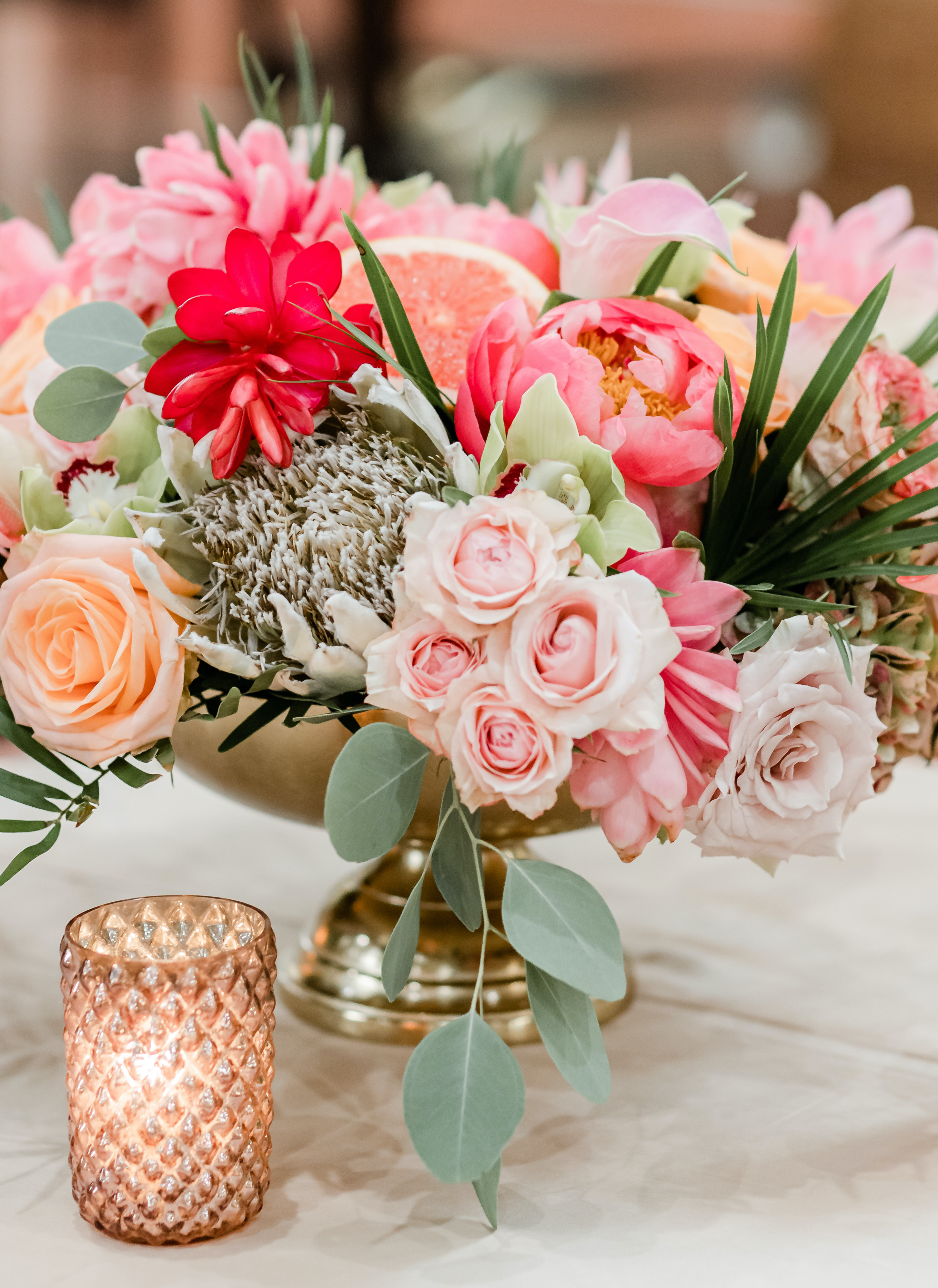 A tropical centerpiece full of bright pink, orange and red flowers sits on a table for a wedding reception.