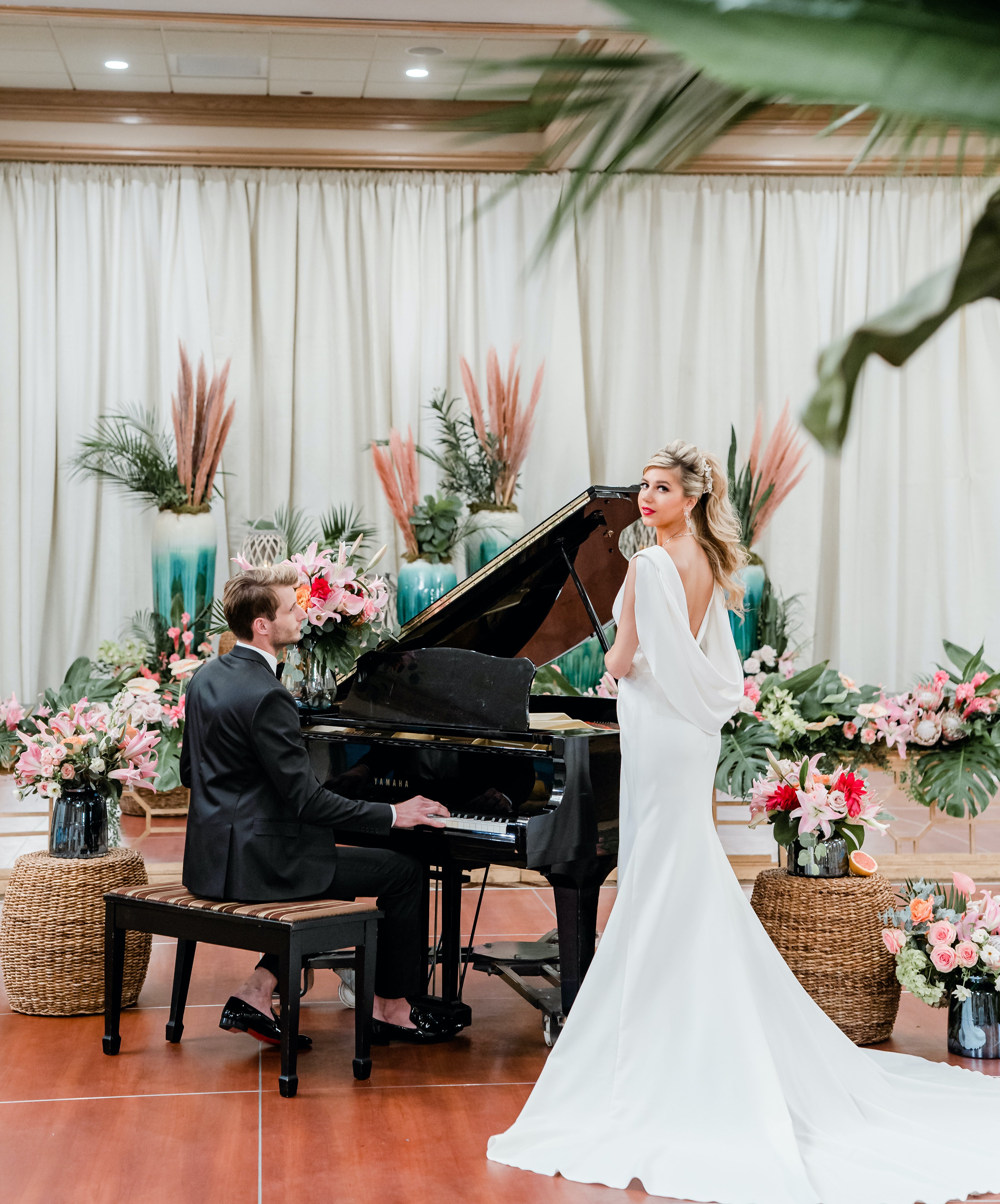 A groom plays the piano while the bride stands next to him and looks at the camera during their tropical wedding reception at The San Luis Resort, Spa & Conference Center.