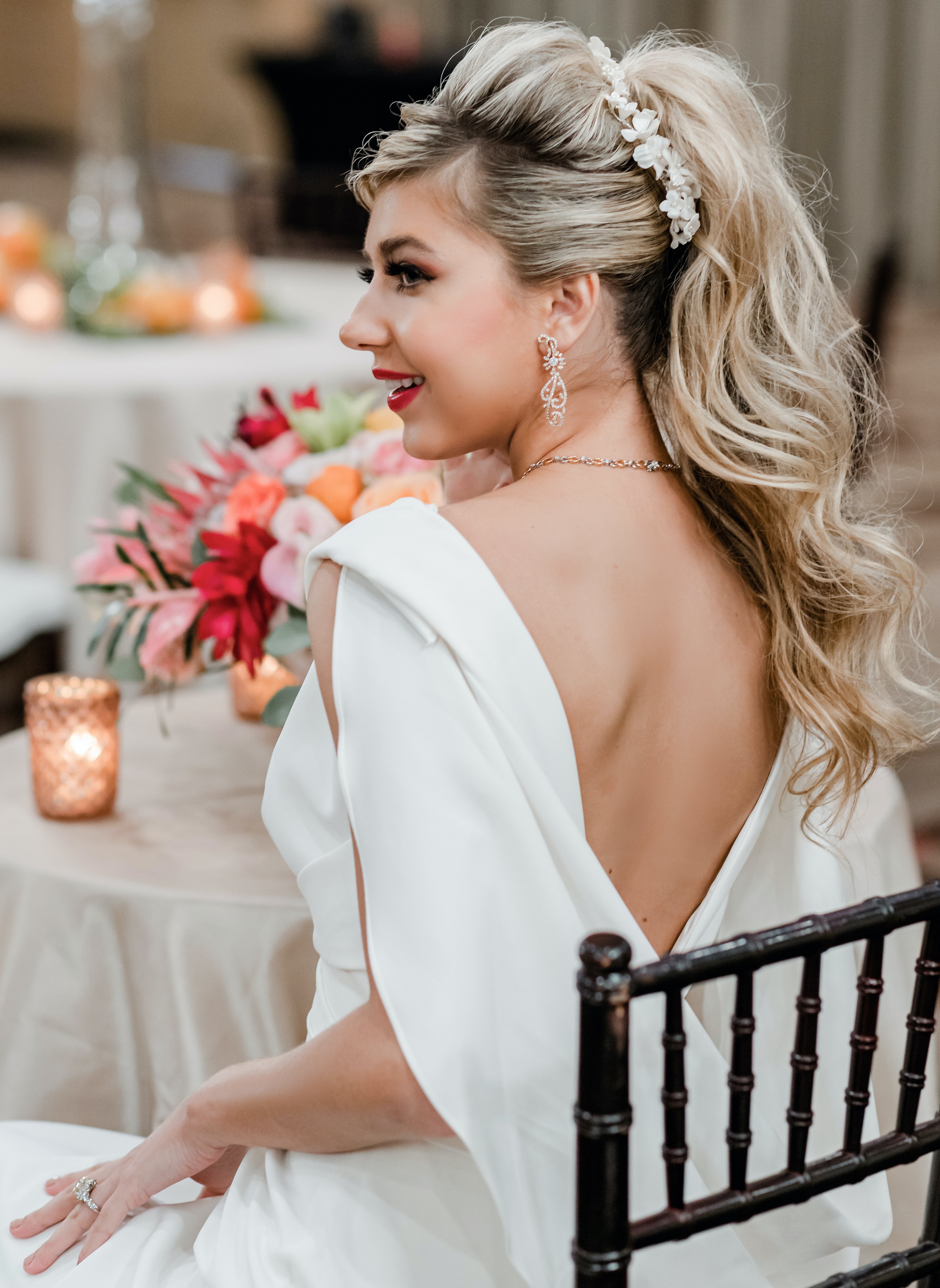 A bride's back is to the camera as she looks to the side. Her hair is in a curly high ponytail with a flower comb tucked within it.