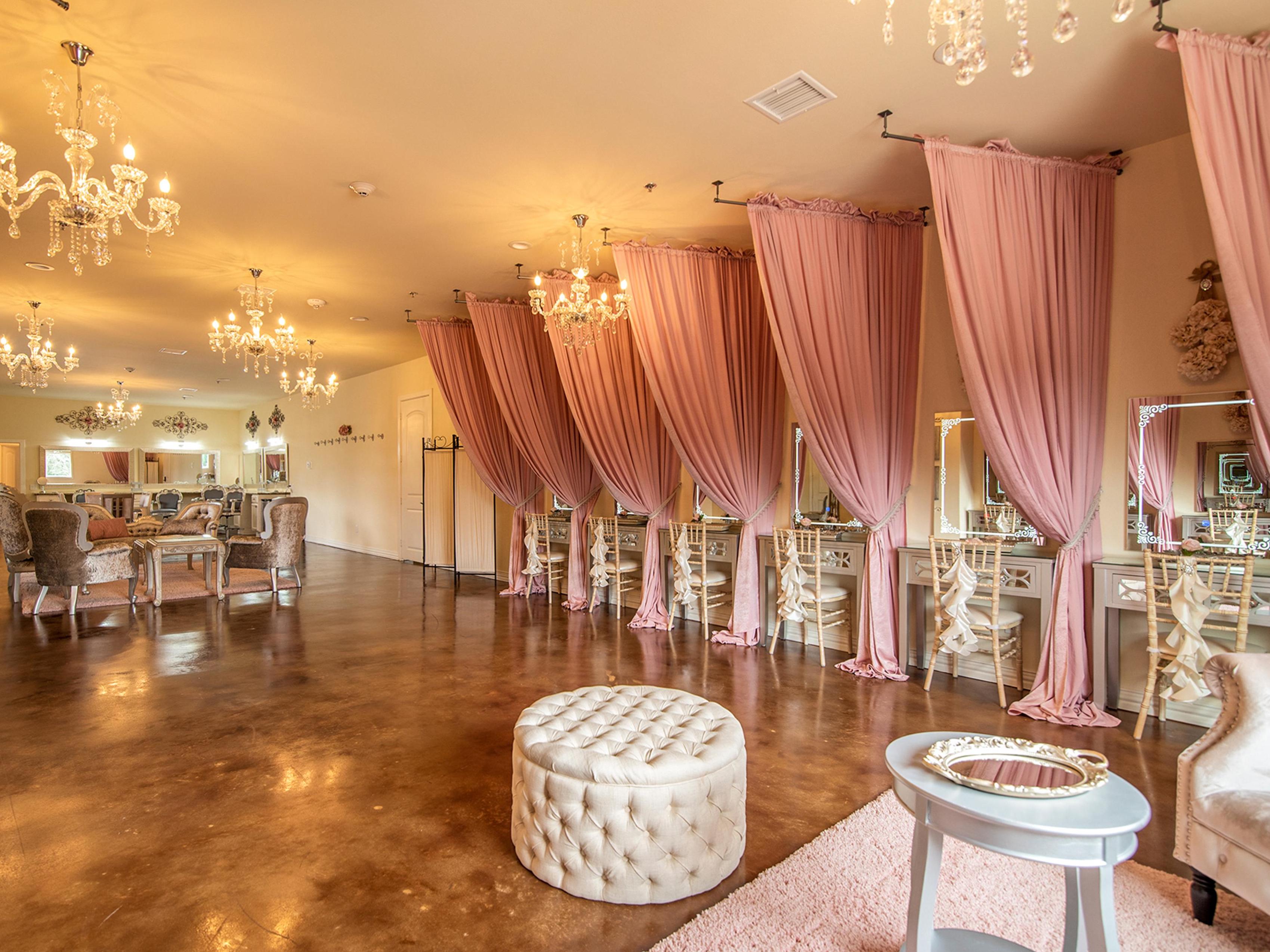The bridal suite in The Hundred Oaks wedding venue has crystal chandeliers and mauve pink drapes with several vanities on the right side.