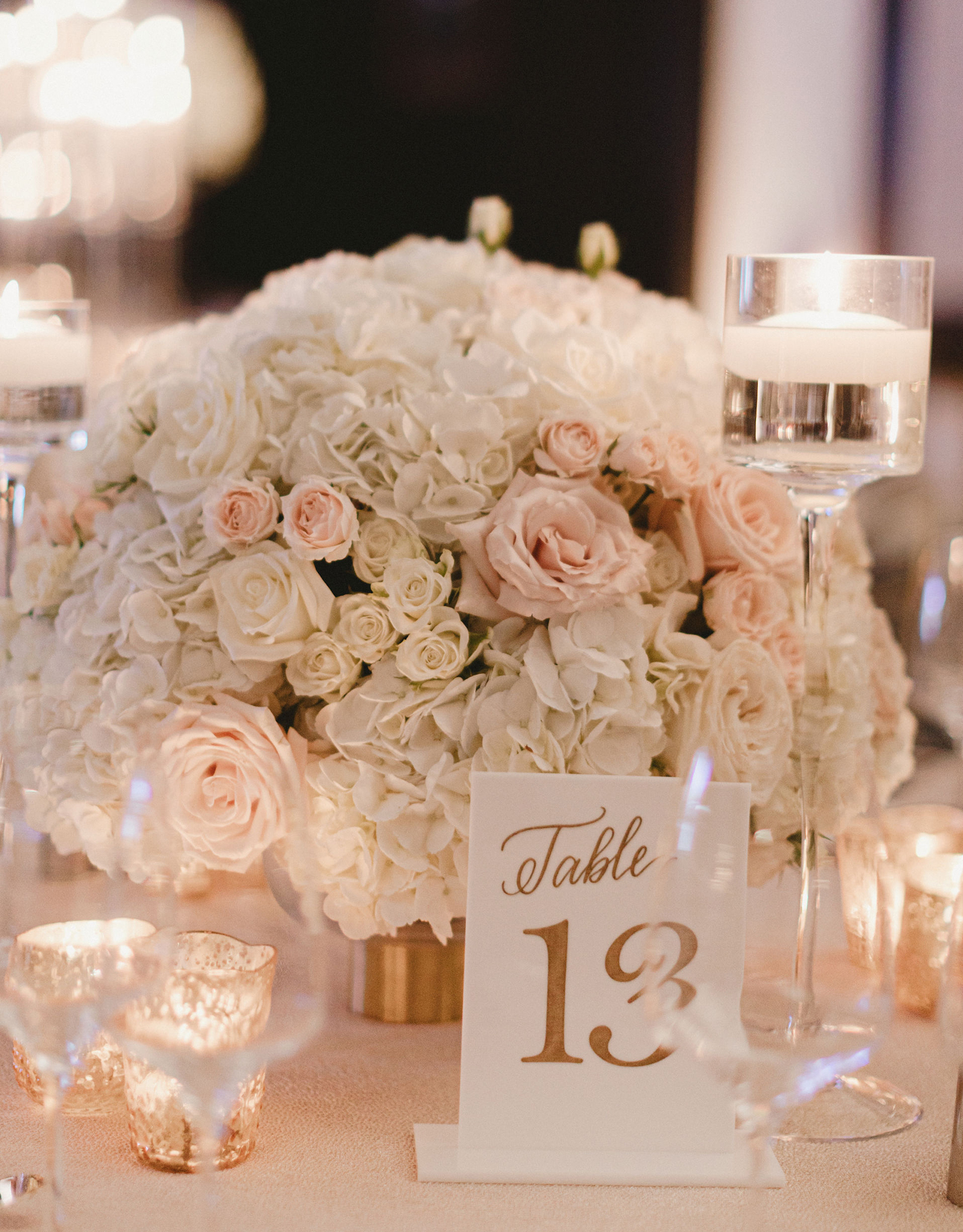 A wedding ceterpiece is filled with white and pink flowers and surrounded by candles and gold accents for a romantic ballroom wedding in Houston.