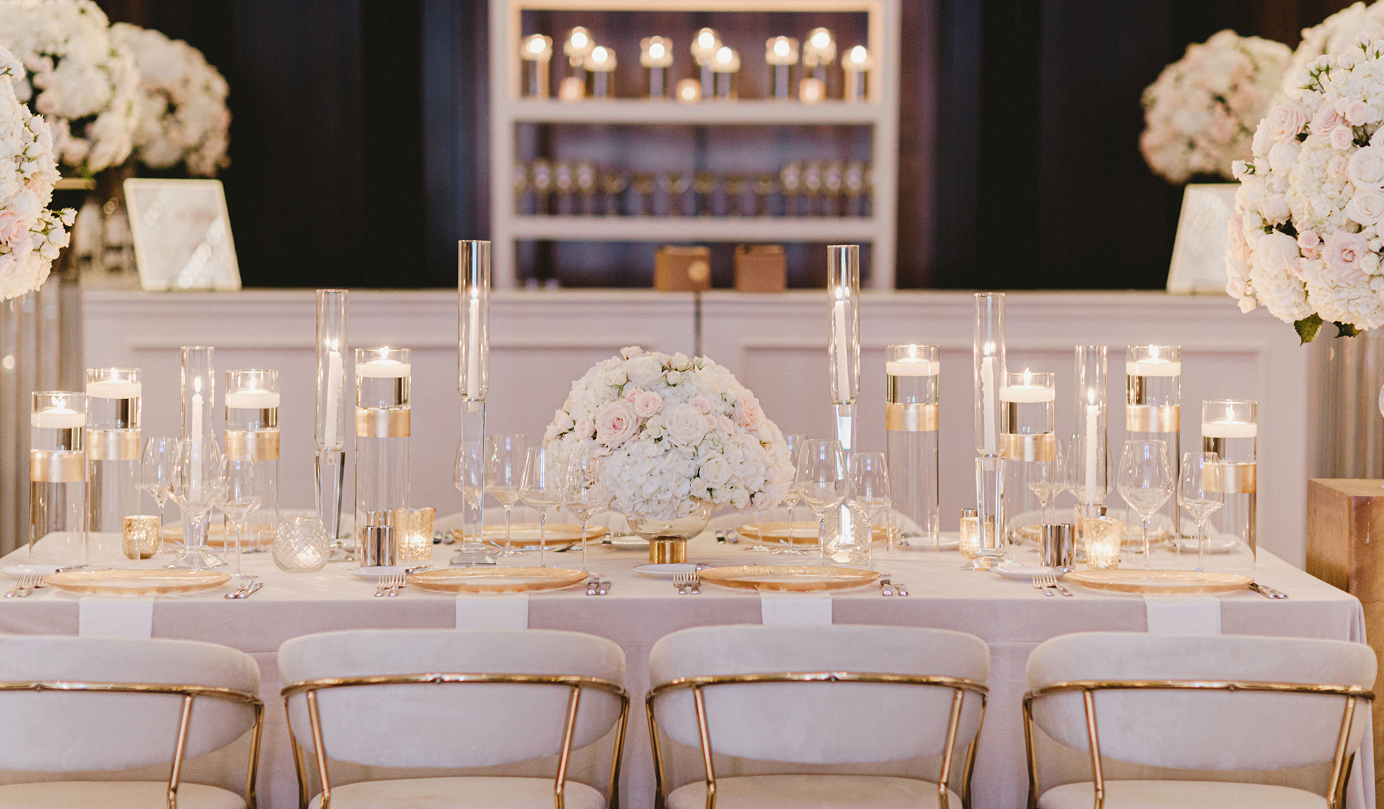 A wedding reception table is set up with elegant candles, white flowers and gold accents for a romantic ballroom wedding at The Post Oak Hotel in Houston, TX.