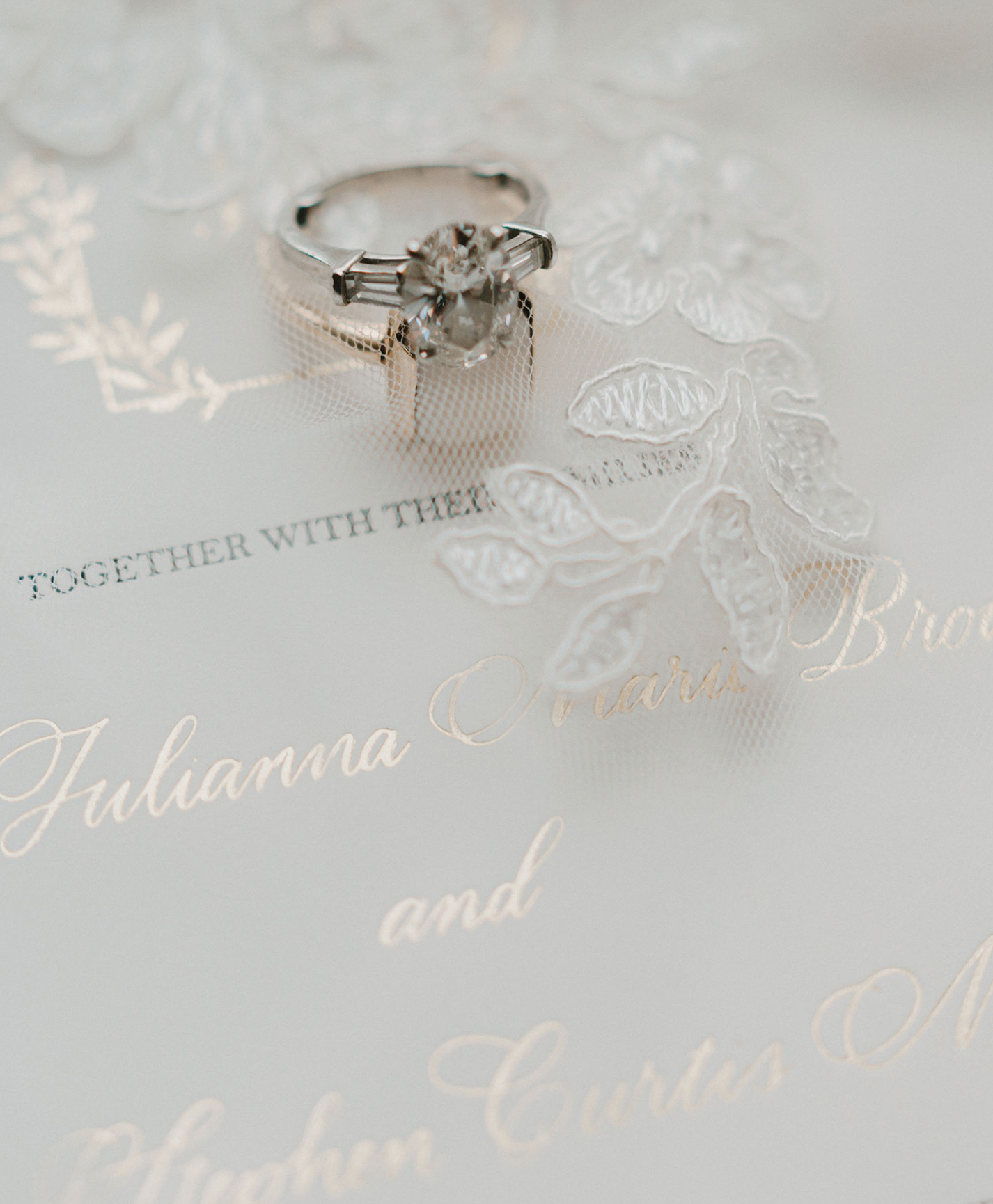 A silver engagement ring with an oval diamond sits on a wedding invitation for a wedding at The Post Oak Hotel in Houston.