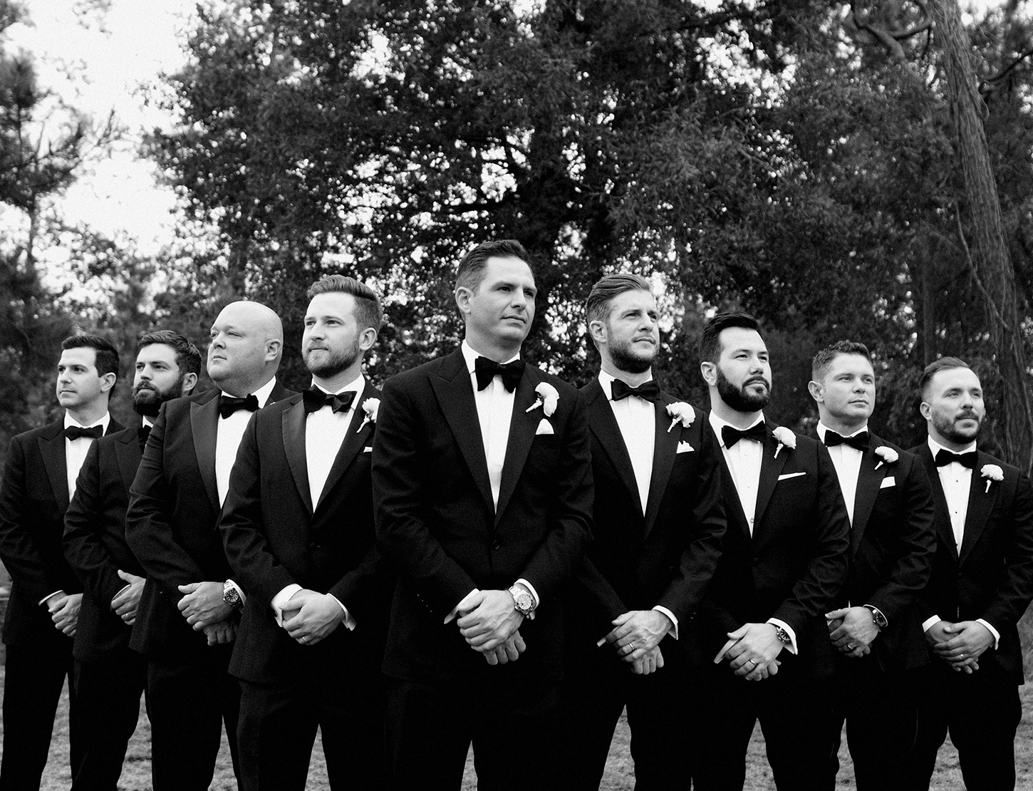 A black and white photo of a groom standing with all of his groomsmen before his romantic ballroom wedding in Houston.