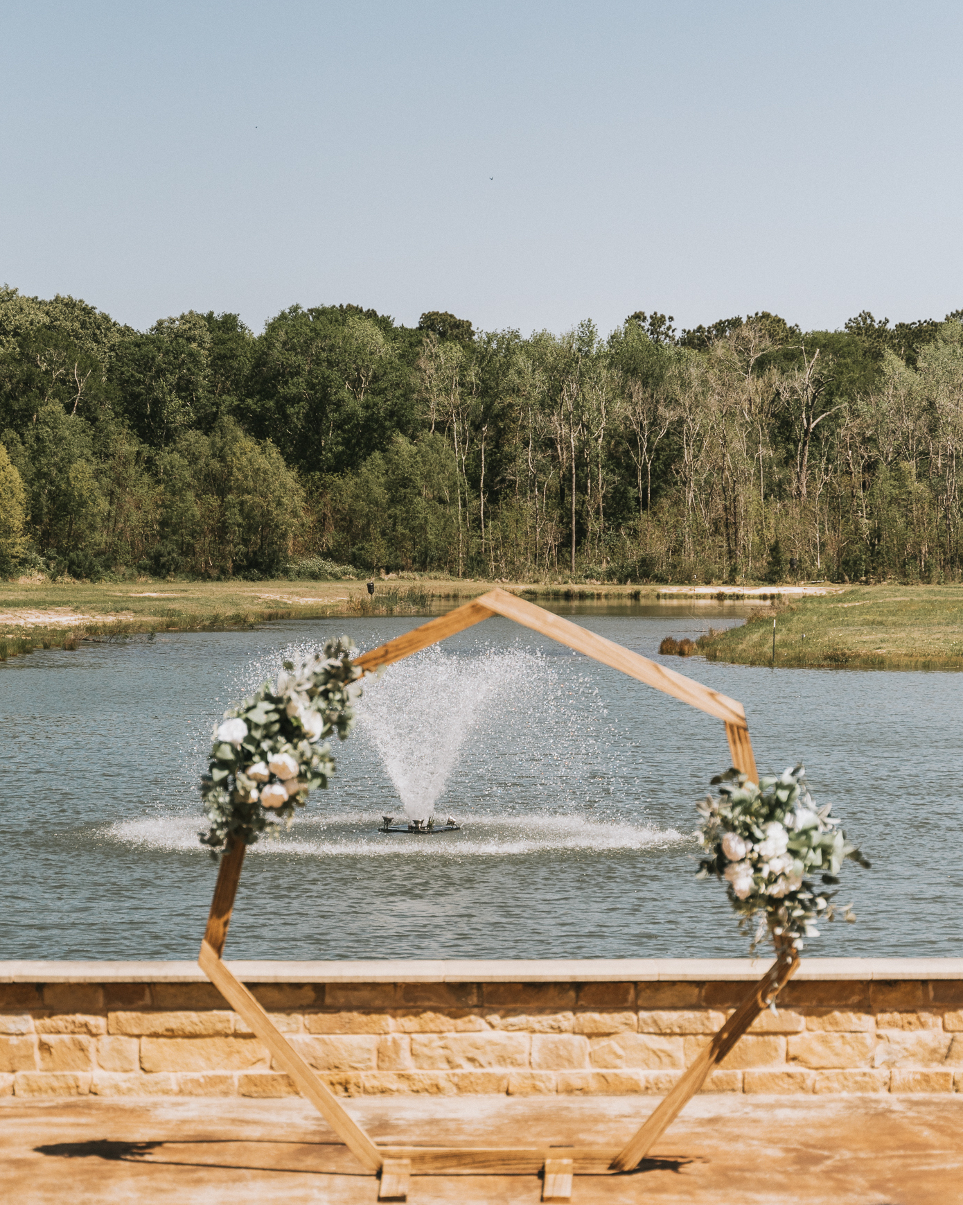 A pond is the view through an archway decorated with greenery and flowers at a secluded luxury venue called The Hundred Oaks Event Center.