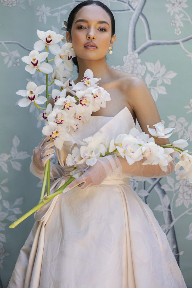 Woman holding four large stems of orchids wearing a strapless blush wedding dress by Anne Barge. English Garden Inspired