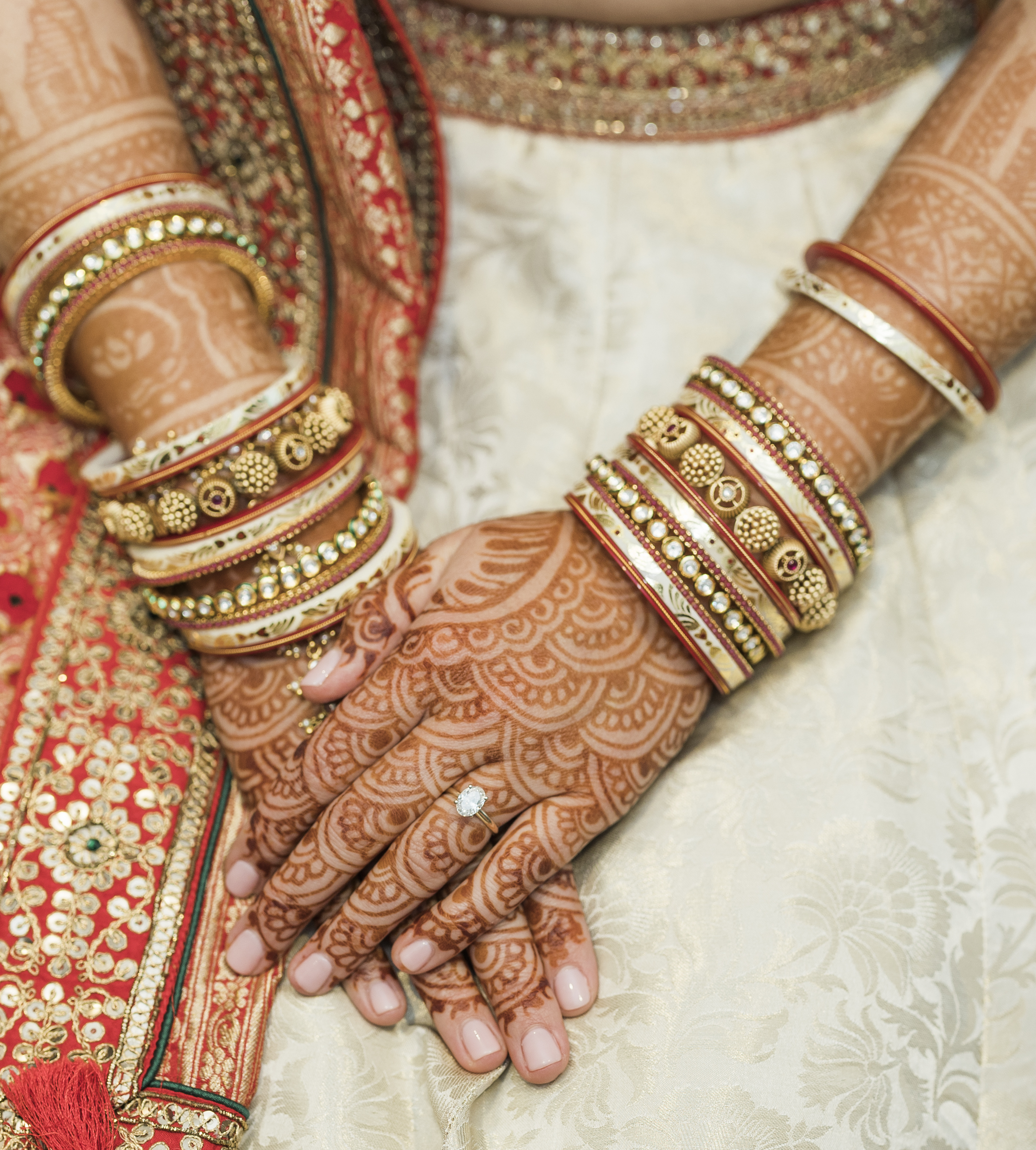 A bride's hands decorated with bridal henna, gold and red bangles and a diamond engagement ring at her indian-fusion wedding in North Houston. 