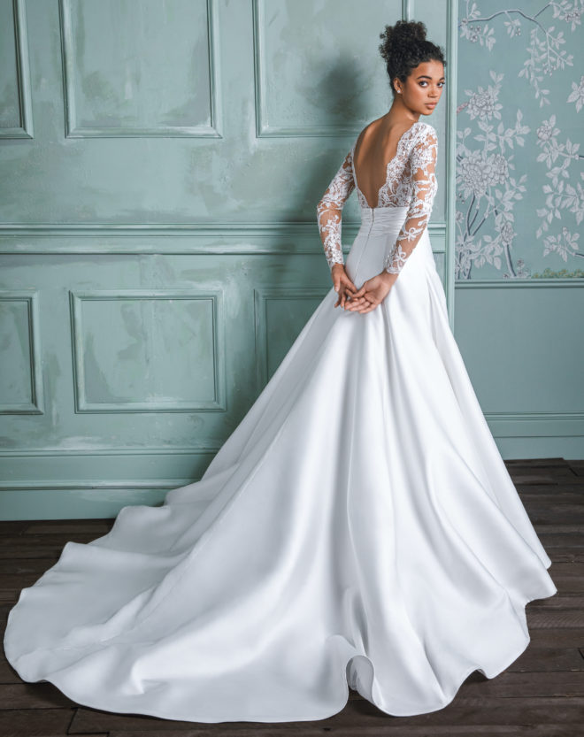 Model in a white ballgown with long lace sleeves, full skirt and long train from the 2023 bridal collection by Anne Barge. 