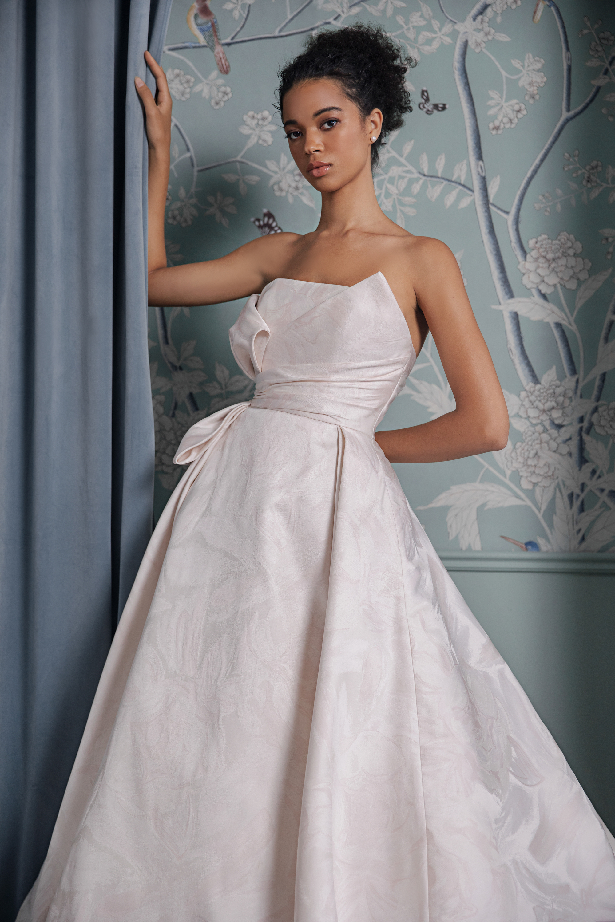 Model in strapless a-line wedding dress with full pleated skirt and bodice drape by Anne Barge. 